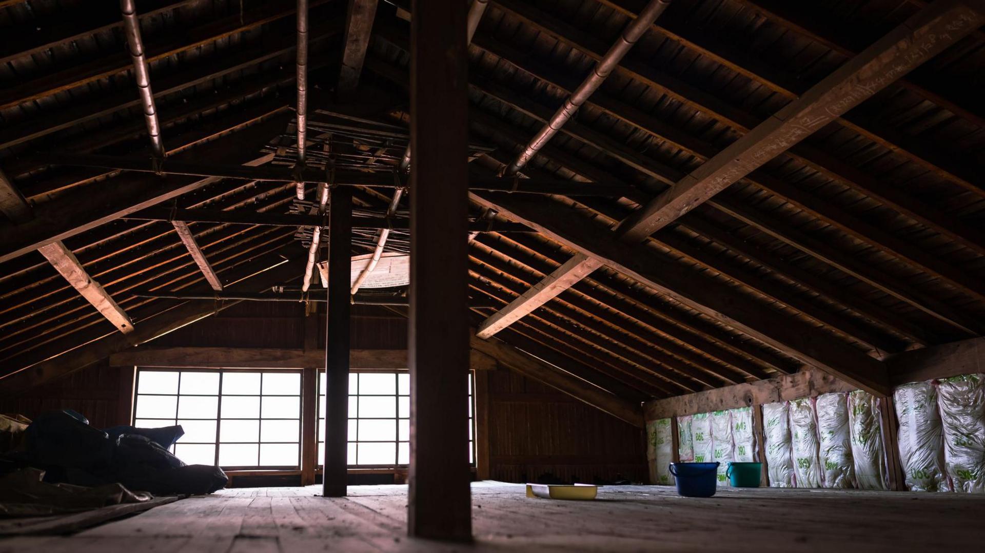 A dark attic with wood wooden beams, lit only by a small window 