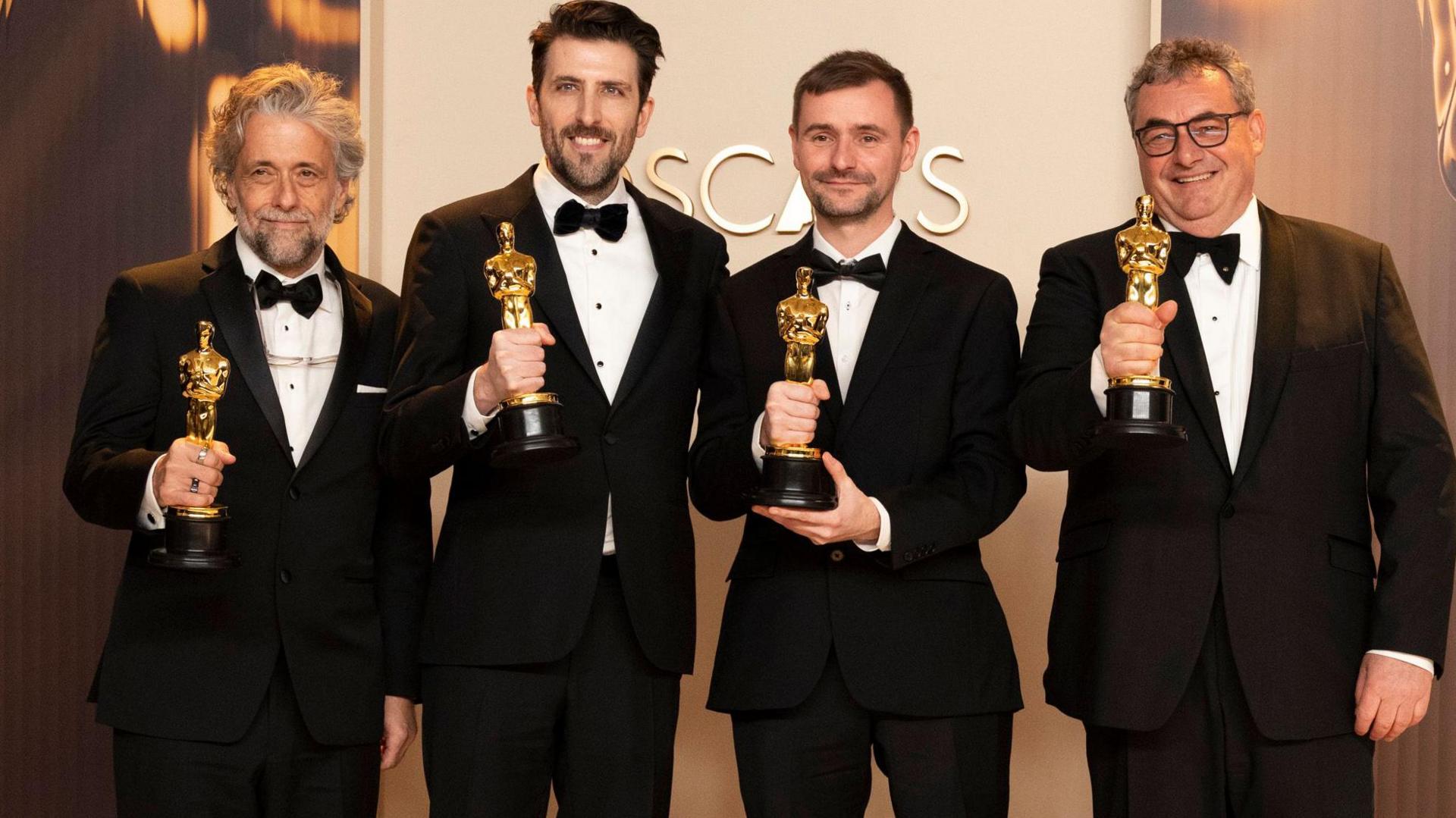 Paul Lambert, Stephen James, Rhys Salcome, Gerd Nefzer collecting their award at the Oscars ceremony. They are wearing black tuxedos.
