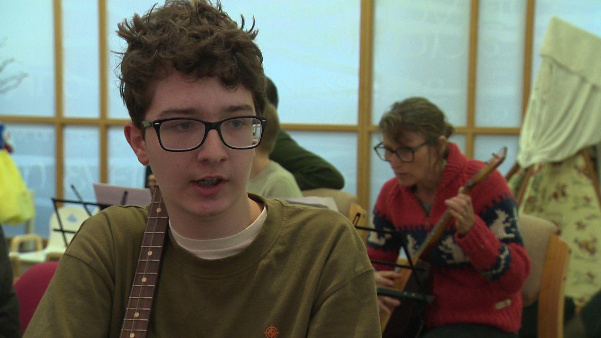 Albert, wearing a green jumper and black framed glasses, pictured talking about his love of the balalaika.