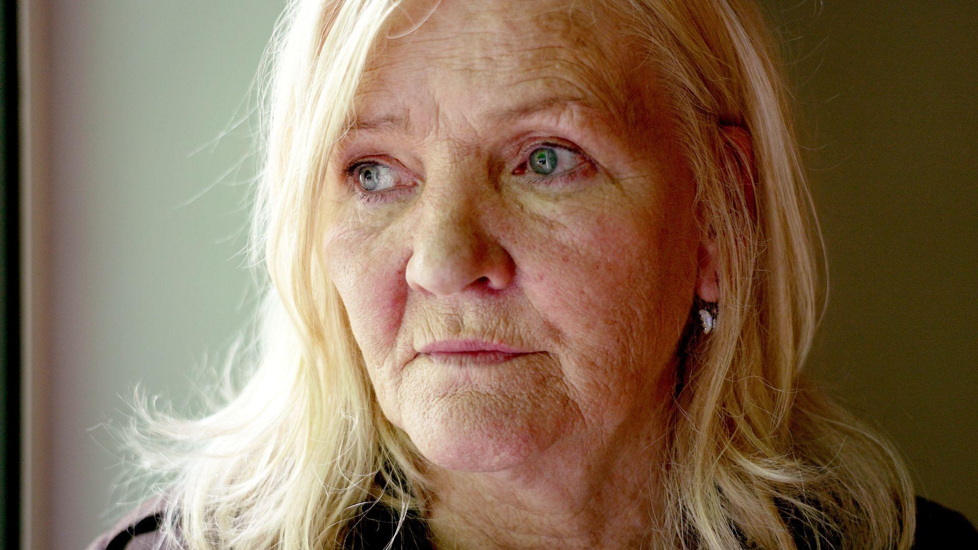 A close-crop of Catherine looking into the distance. She looks serious and pensive and her blonde shoulder-length hair is half in shadow.