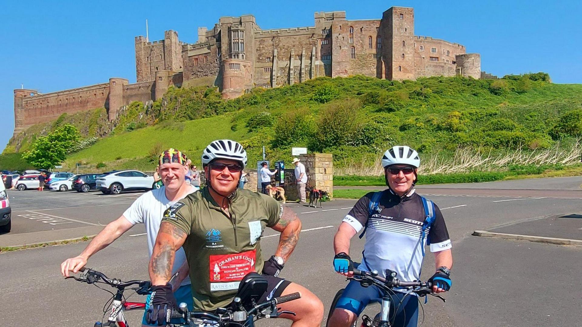 Jamie Bell (centre) and friends, Angus Intini and Steve Charlton, posing on their bikes in front of Bamburgh Castle, Northumberland