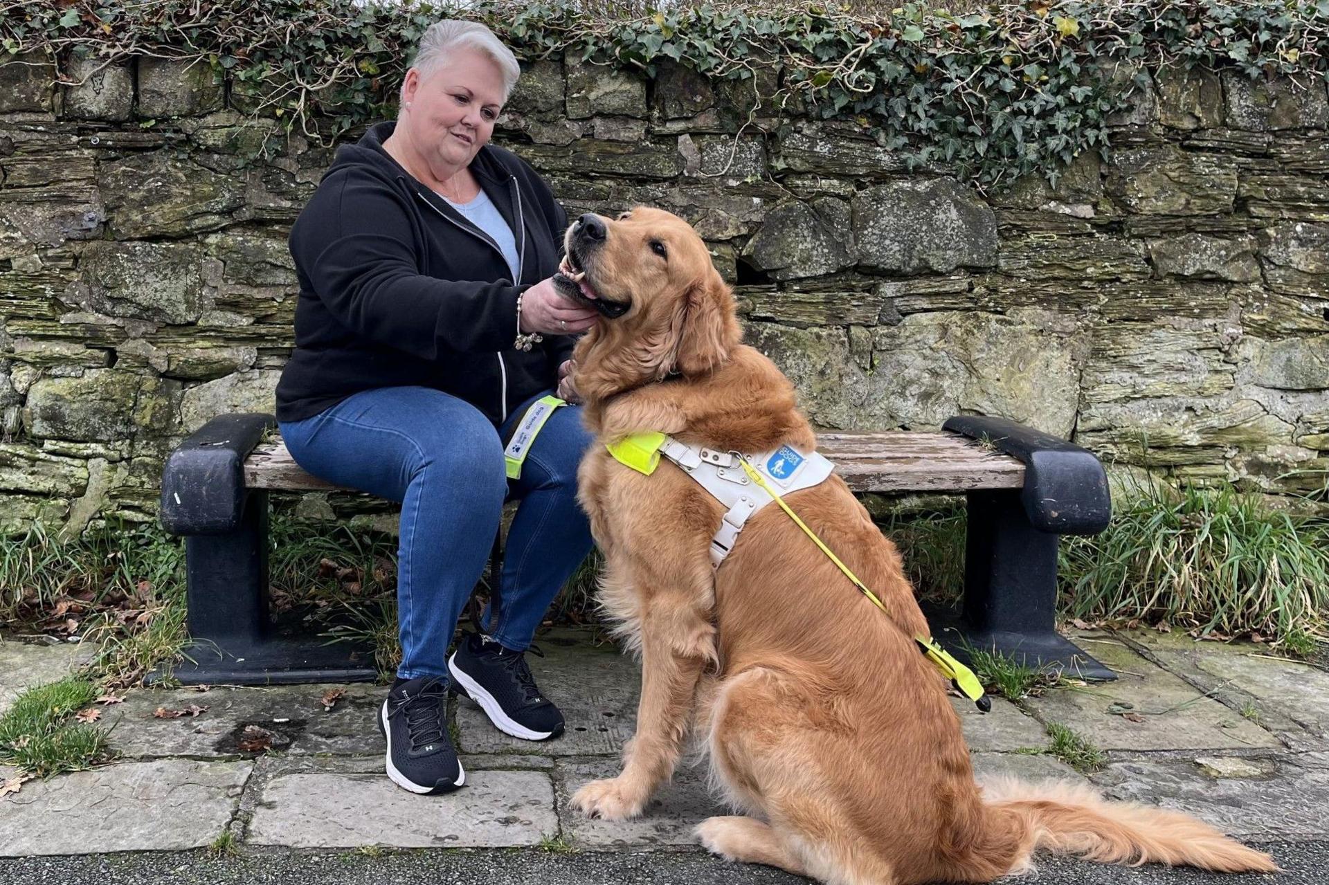 Woman sits on bench next to a guide dog 