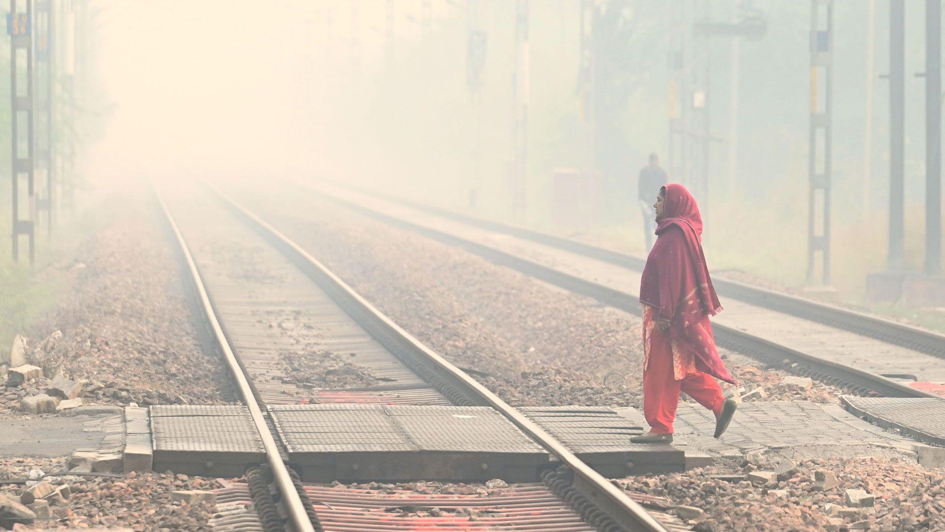 Smog engulfing railway tracks in Delhi on 13 November 2025 in New Delhi, India, as a woman wearing a red Indian outfit, with her head covered walks by.