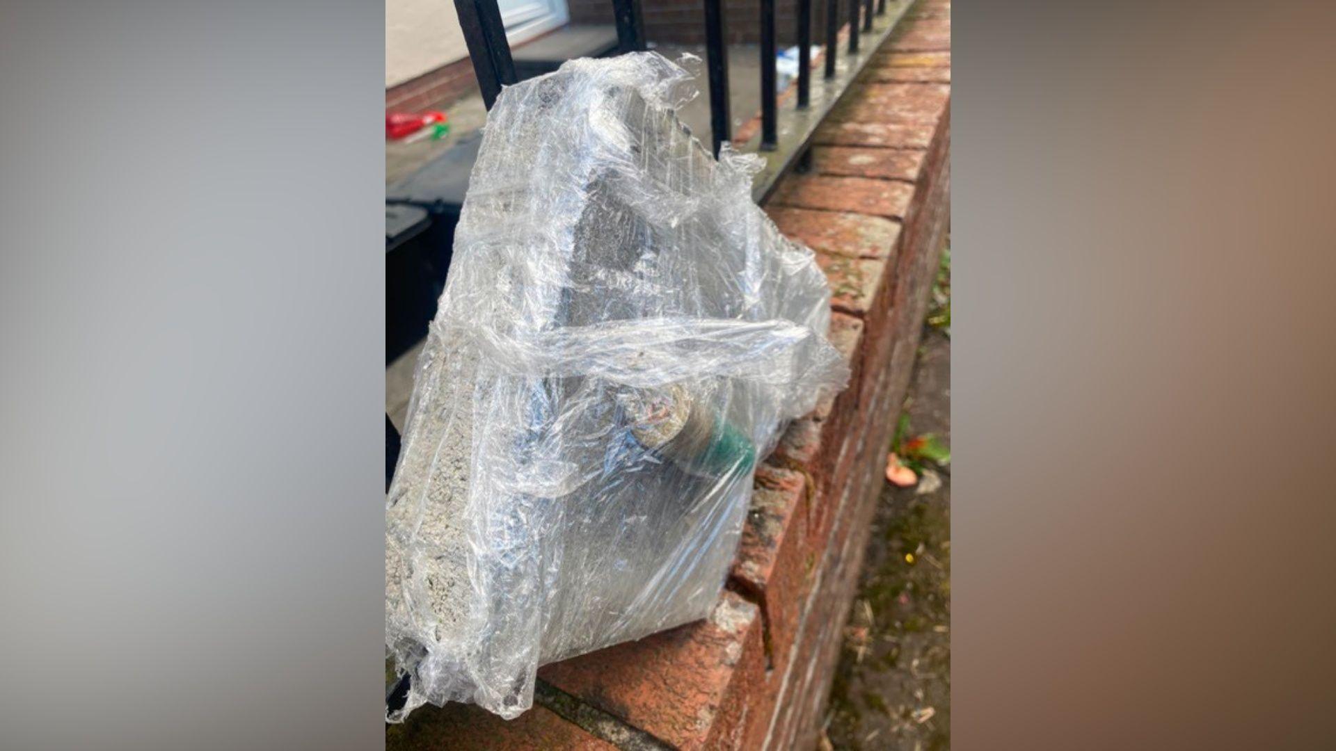 What appears to be a bullet casing and a brick wrapped up in clingfilm on a wall
