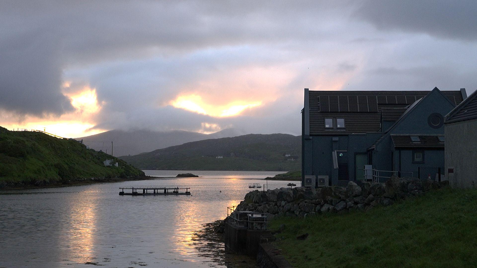 Talla Coimhearsneachd Scalpaigh agus a' ghrian a' dol fodha air a cùlaibh.