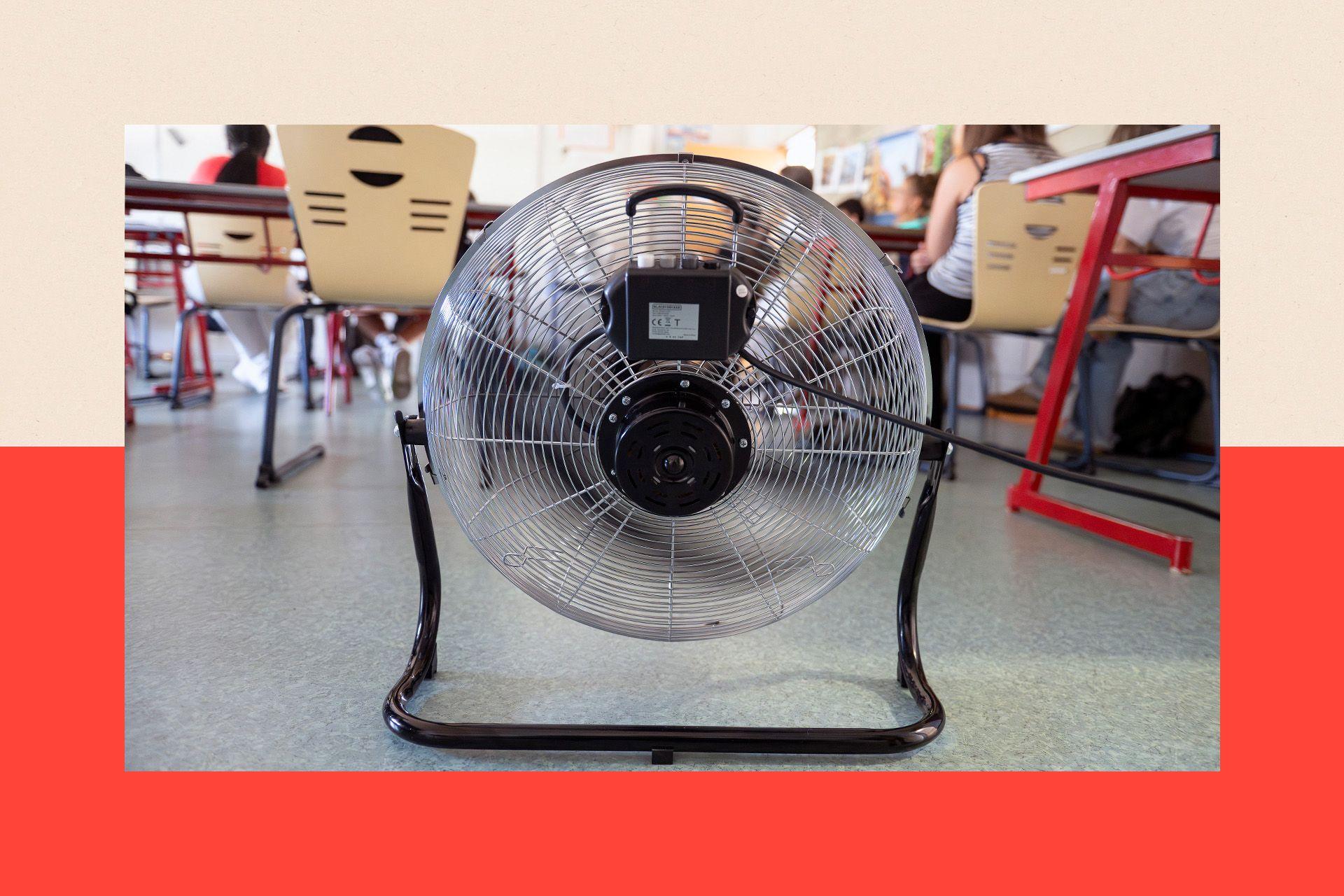 Close-up of a fan cooling pupils in a classroom in Poitiers, France. Chairs, tables and the backs of pupils are also visible. There is a red and beige backdrop.