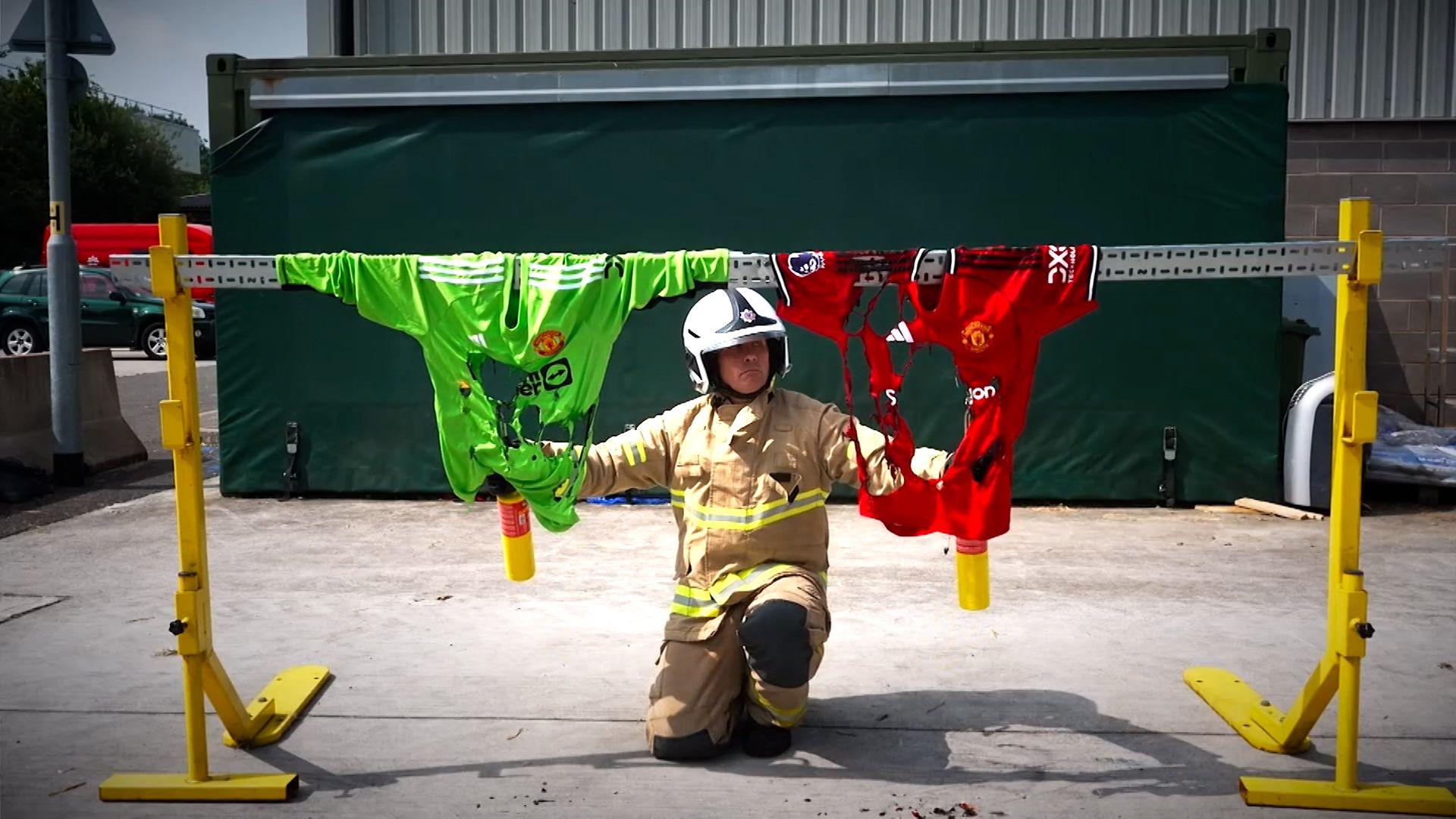 Cheshire Fire and Rescue Service watch manager Dave Jackson kneels below an iron bar which has two football shirts hanging from it. he has two blow torches and set them on fire. On the left, the green strip is an official item, and the red one on the right is fake and has burned more easily.