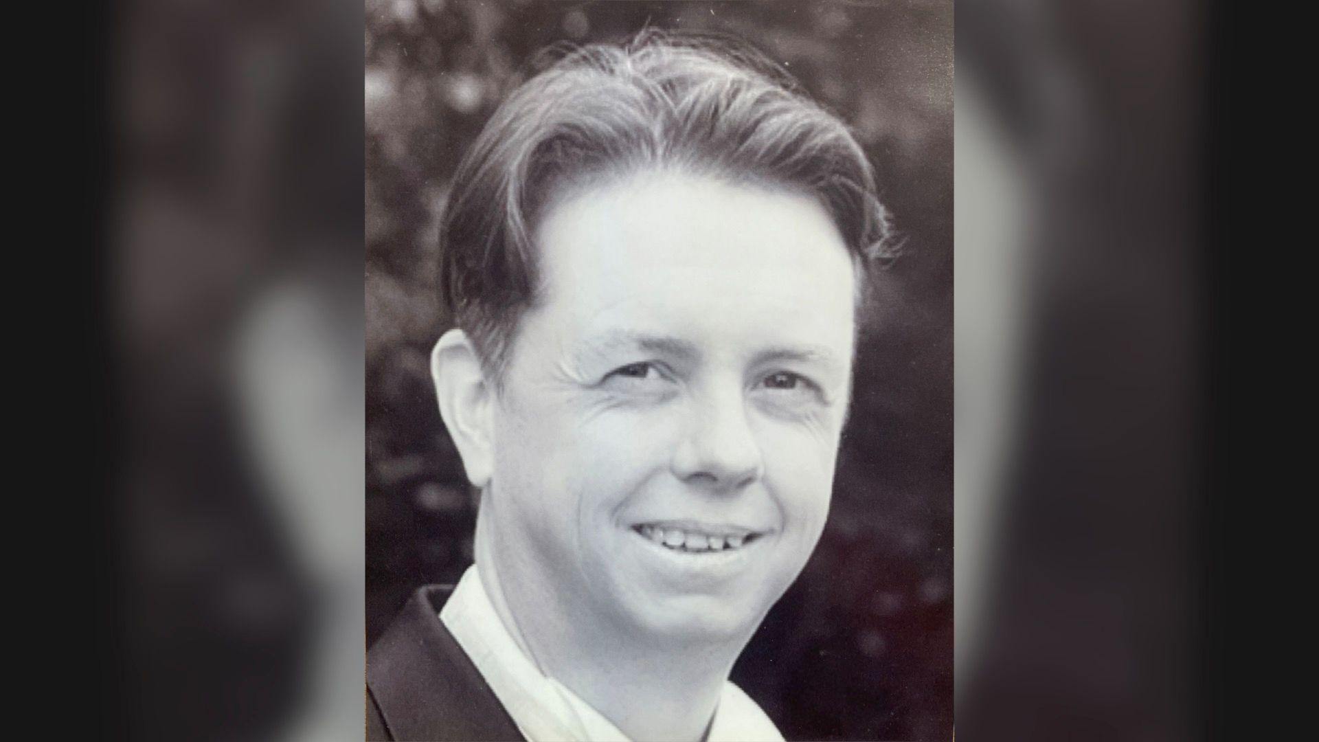 A black and white photograph of Simon Scott wearing a dark suit and a white shirt