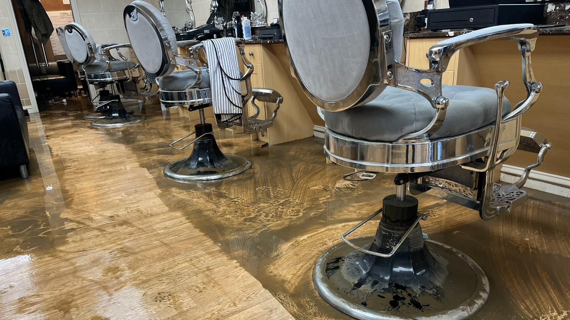 A barbershop floor is covered in muddy water. Picture shows barber seats and products.