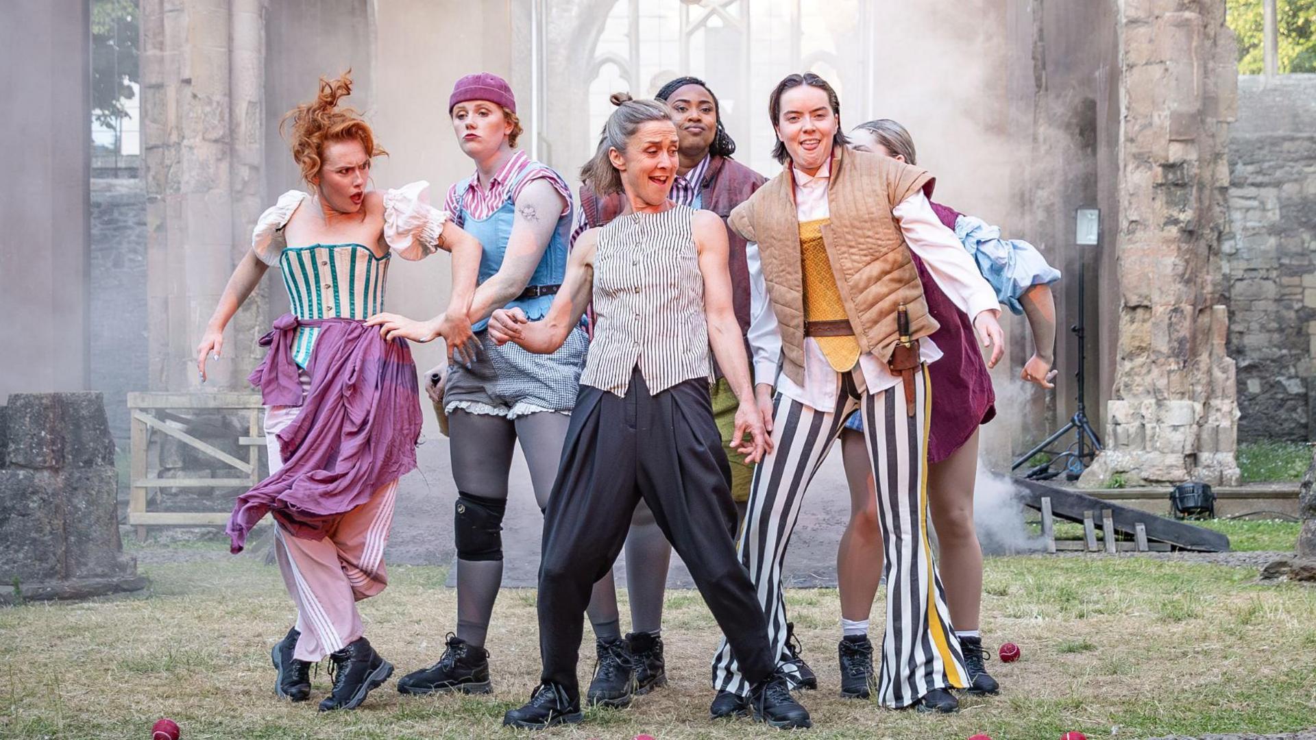 A group of performers stand together in a group in colourful outfits inside the historic Temple Church in Bristol city centre. Behind them the walls of the church are visible