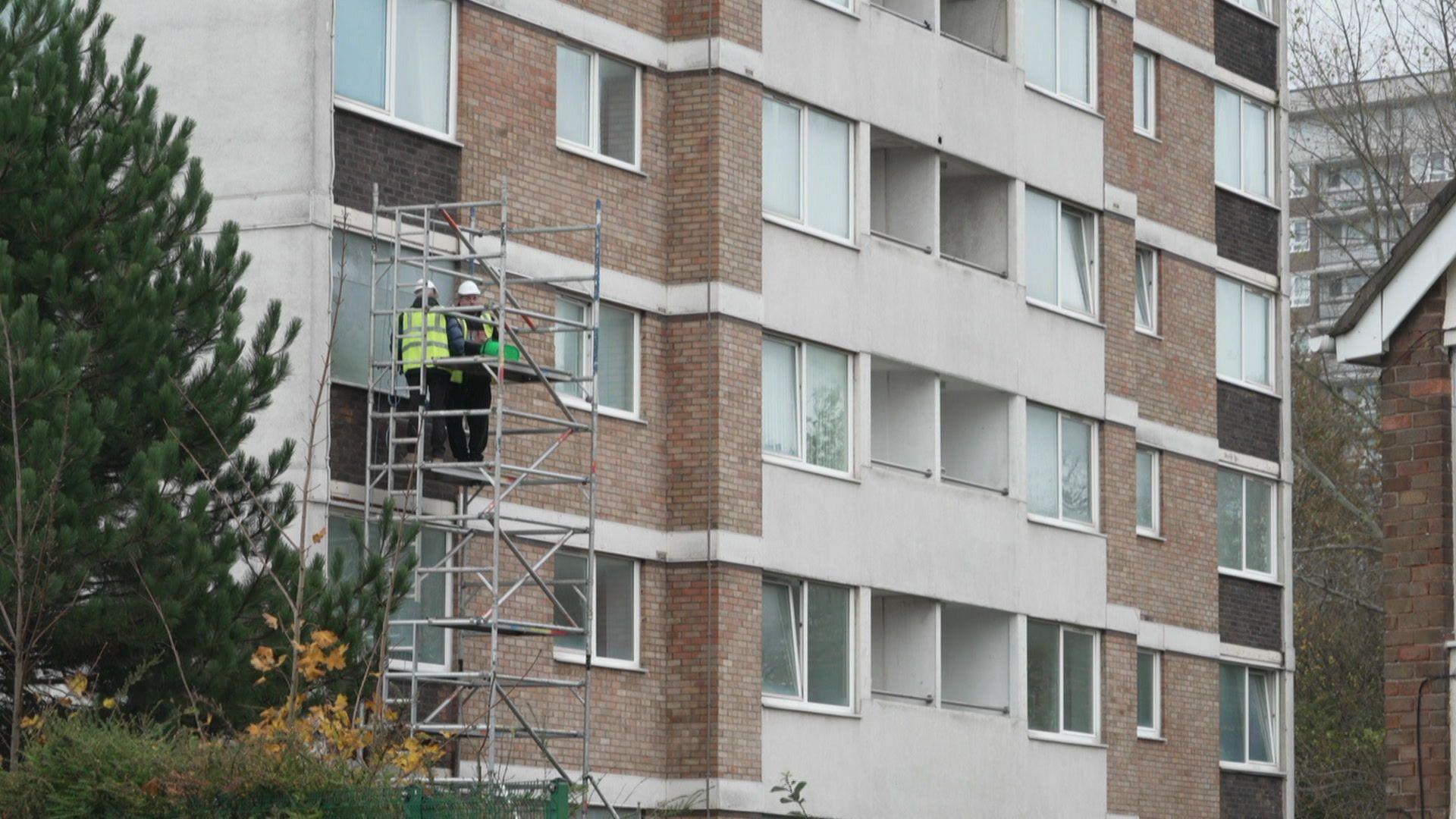 Workmen on a scaffold are tinning up the windows of flats on the lower floors of Beech Rise