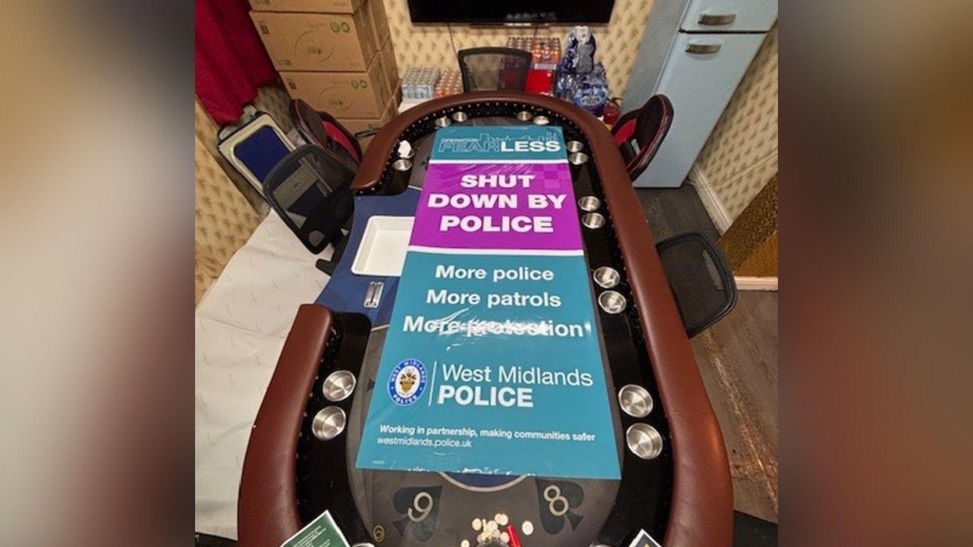 A large oval-shaped card table with a blue and rectangular poster placed on it which says "shut down by police".