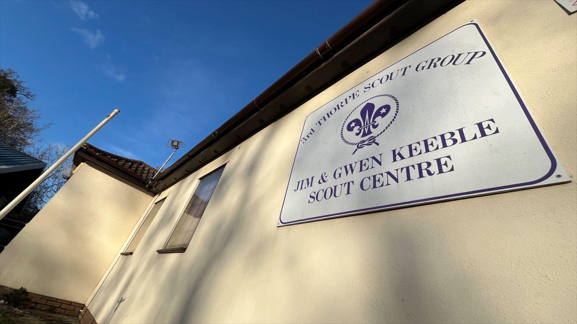 The exterior of the Scout hut building in Thorpe-le-Soken. The walls of the building are rendered and painted cream. There is a large sign on the wall which reads "3rd Thorpe Scout Group, Jim and Gwen Keeble Scout Centre"