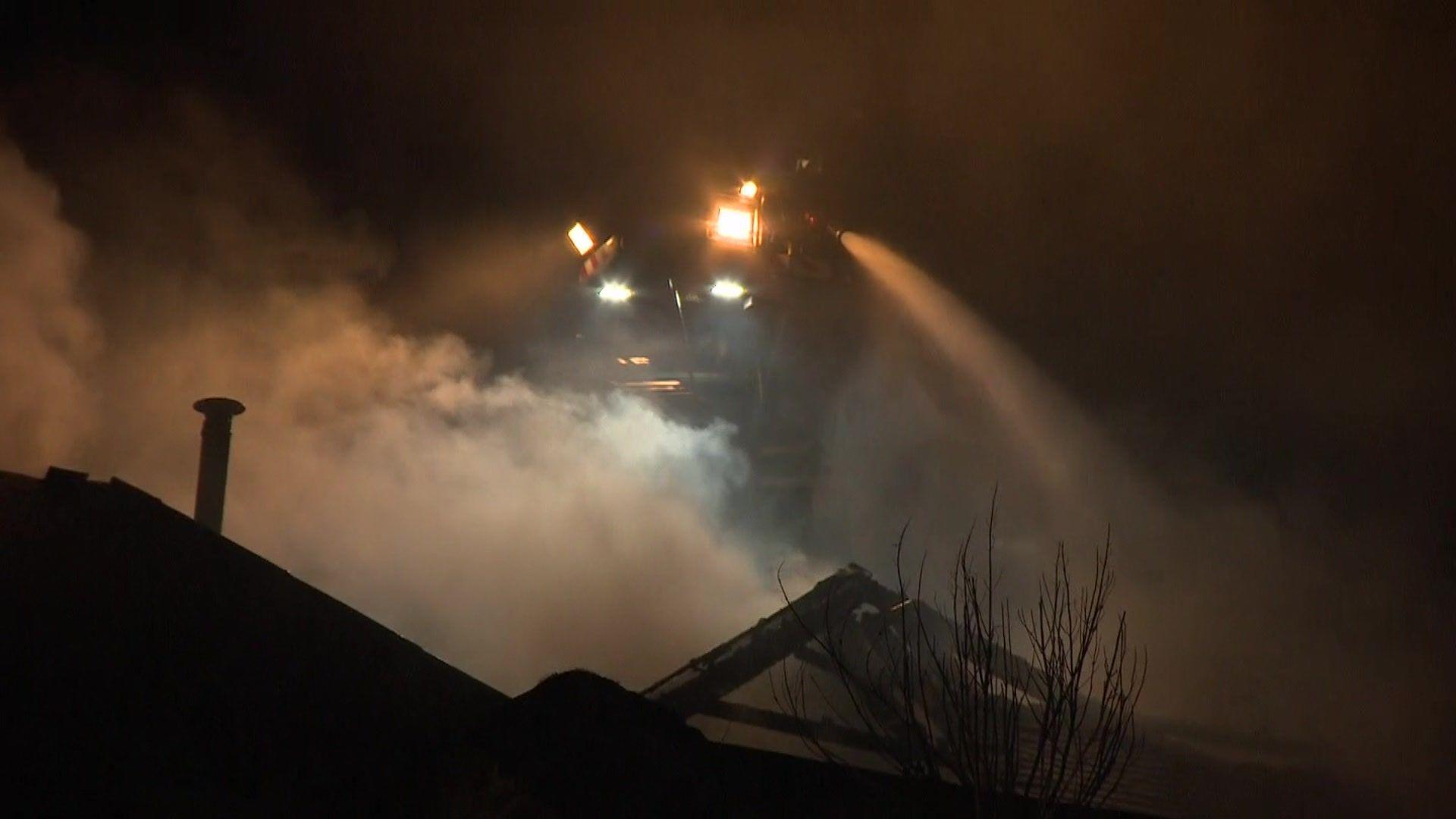 An aerial ladder with fire crew on board sprays water over a smoking building at night.