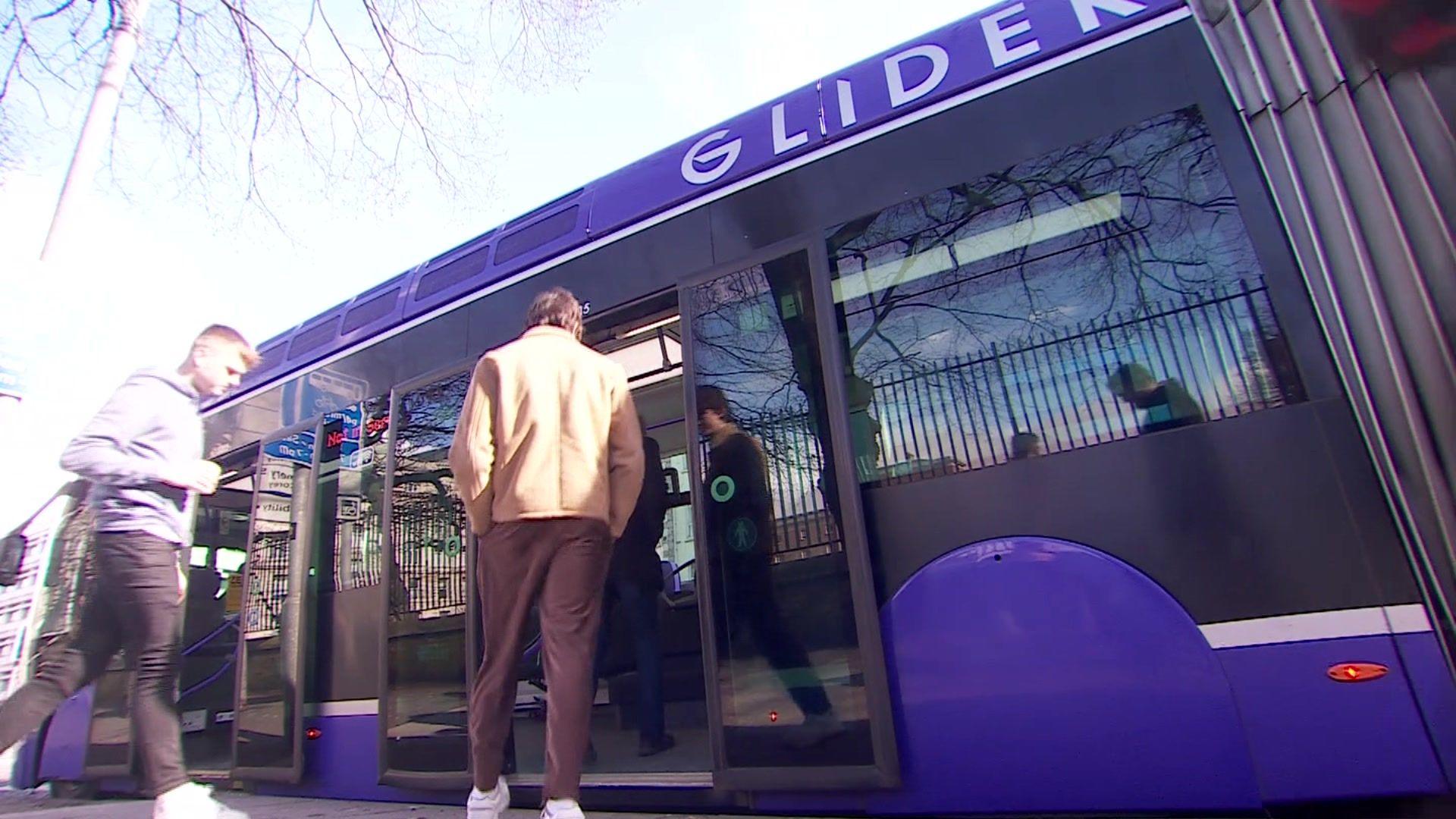 Members of the public get on board a bright purple "glider bus" trackless tram.