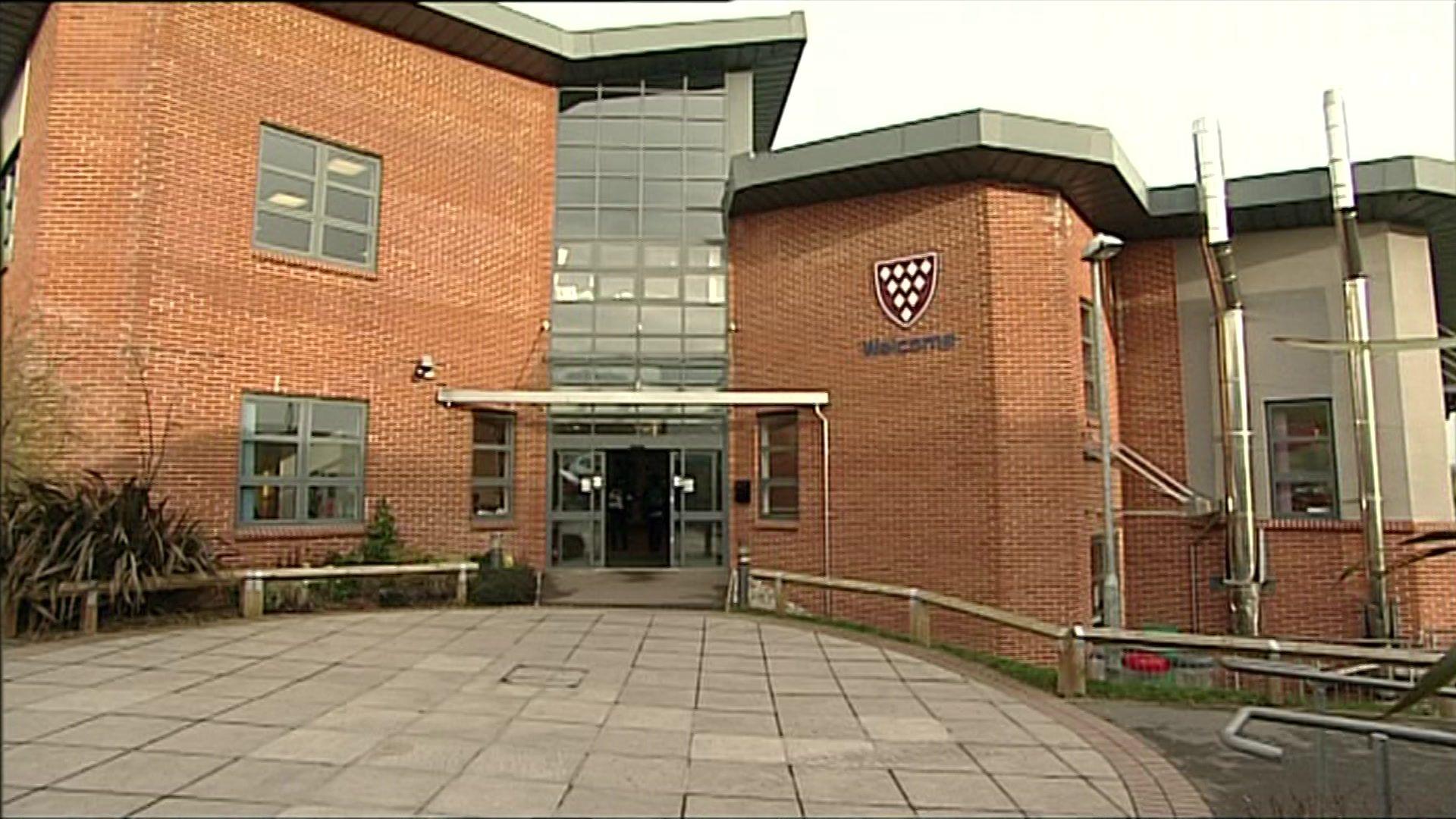 The entrance to Kingsbridge Community College, a large red-brick building, with a curved façade and large glass doors on the ground floor