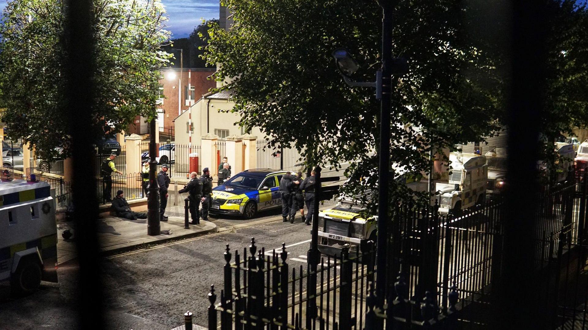 Police officers resting on Bishop Street in Londonderry after coming under attack, One officer with a foot injury is being helped by colleagues.