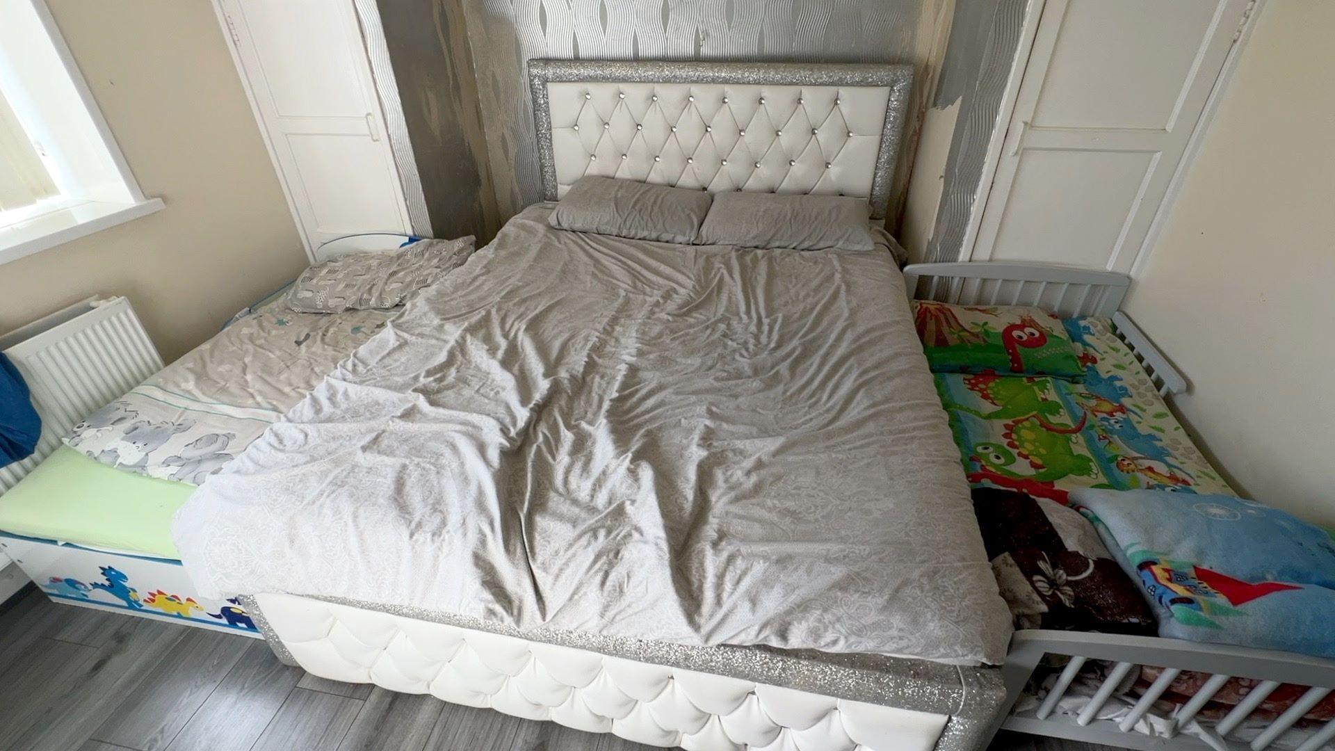 Beds in the home. A double bed is between a cot bed and a small child's bed. There are children's blankets on the cot bed and a dinosaur design on the children's bed. 