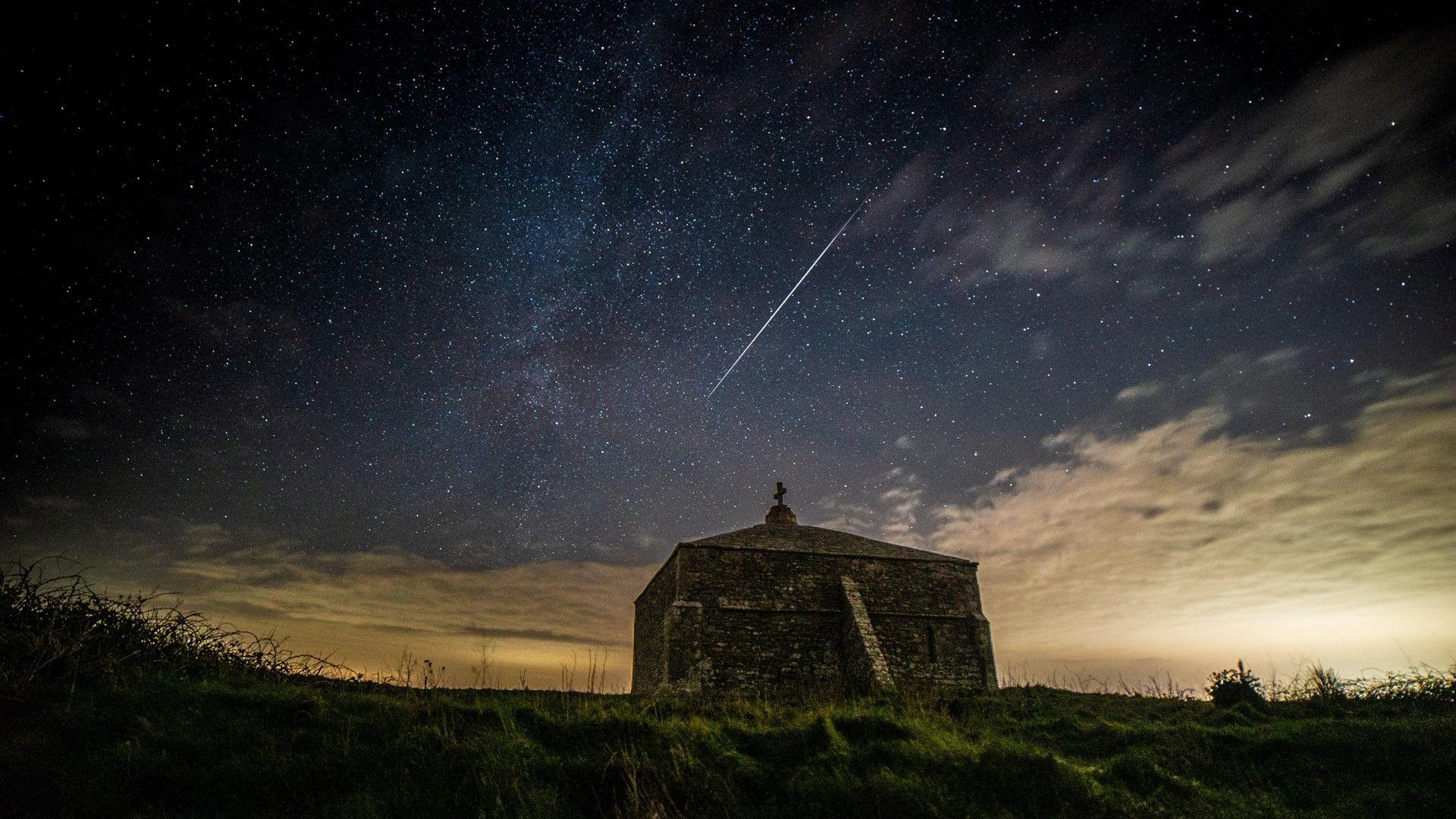 Church building in foreground with a shooting star streaking across the night sky beyond