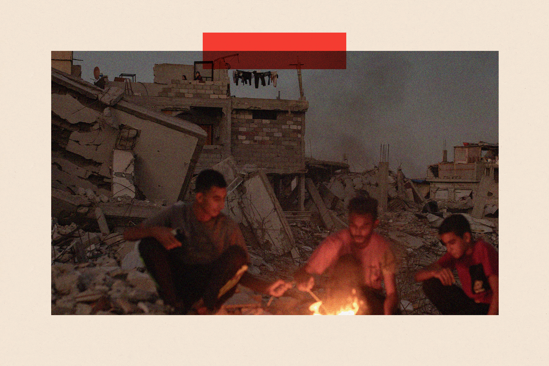 Three men sit by a fire in the debris of a destroyed building