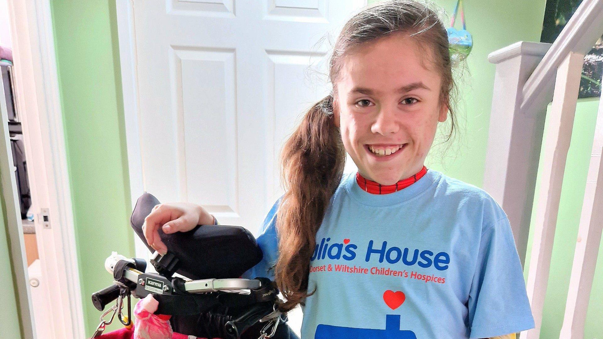 Carmela Chillery-Watson stood in her house, wearing a blue Julia's House t-shirt and stood next to her wheelchair