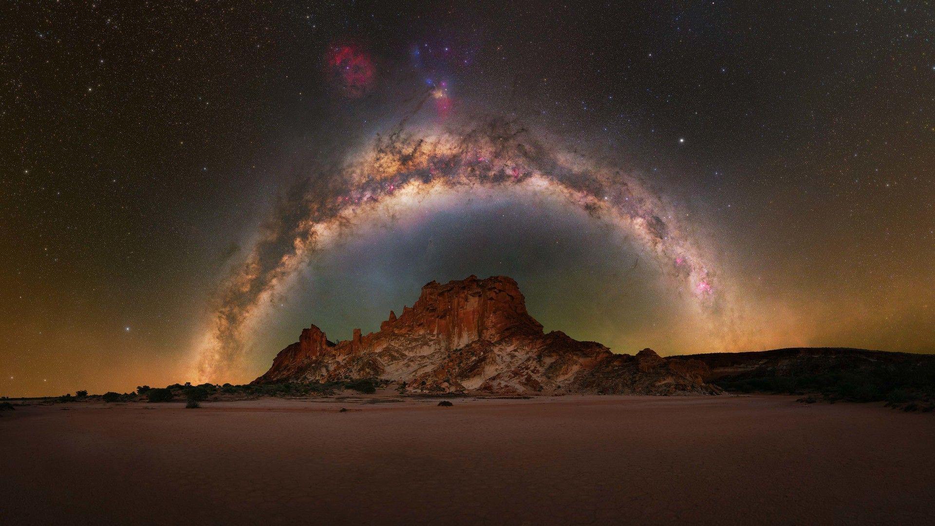 A sandstone rocky hill, with the Milky Way framing it above, in a desert-like landscape