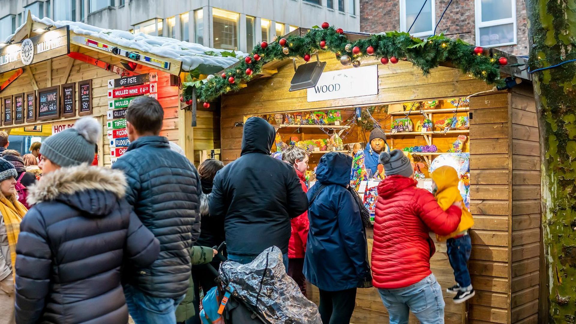 A picture showing wooden Christmas markets stalls with decorations and people shopping outside. 