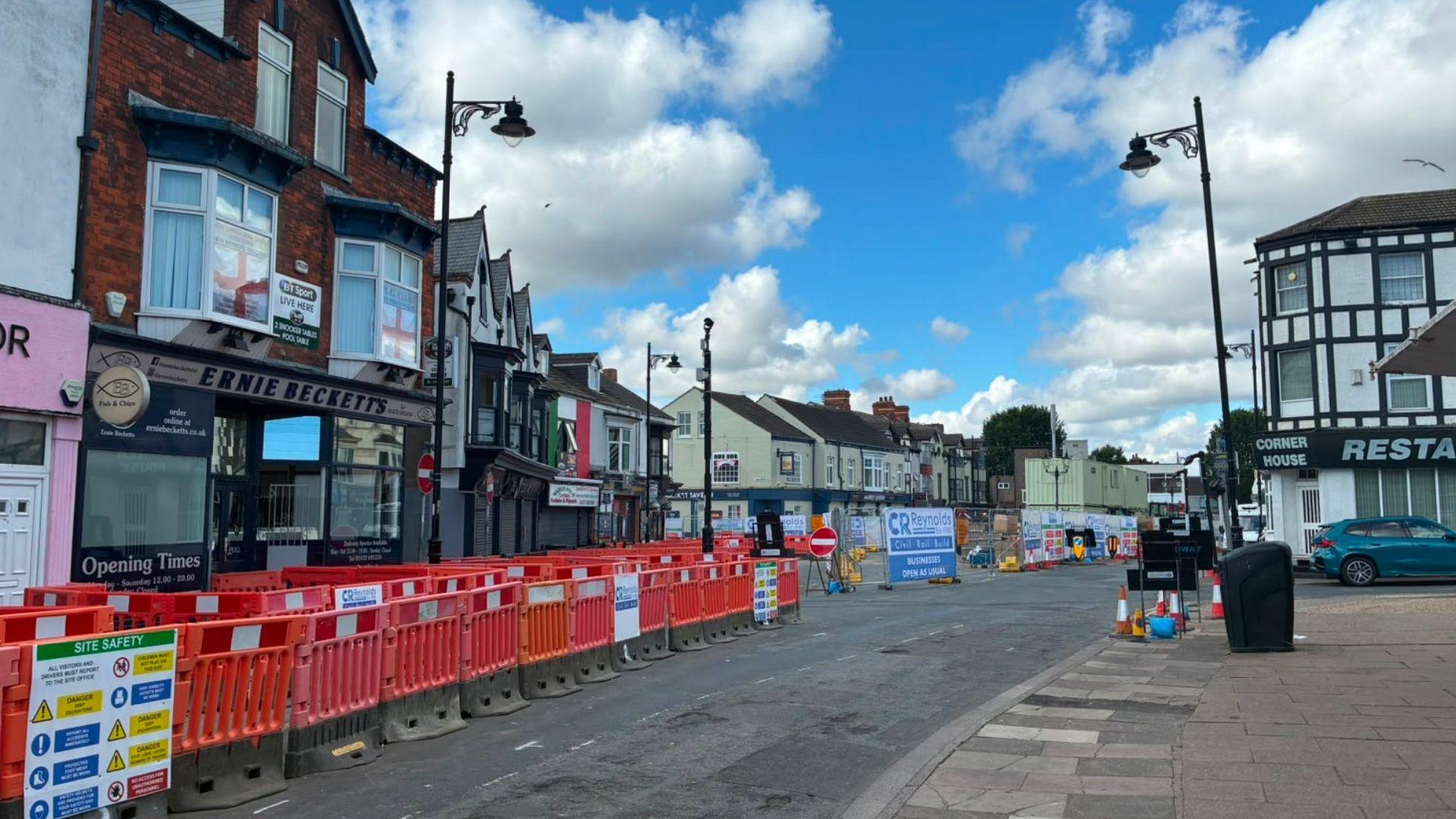 Work on the square with a row of orange and white barriers on one side of the street and traffic cones and road sides at one end