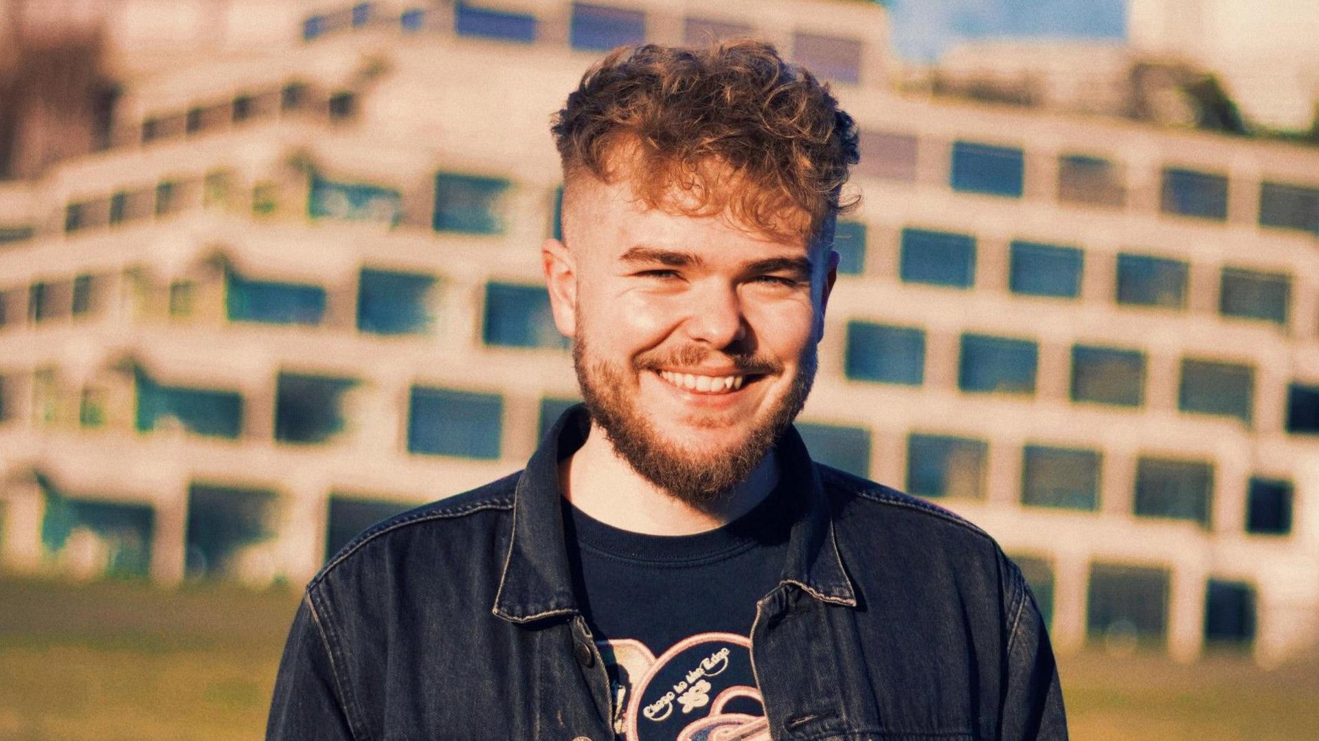 Nathan Wyatt smiling at the camera, wearing a denim jacket and t-shirt