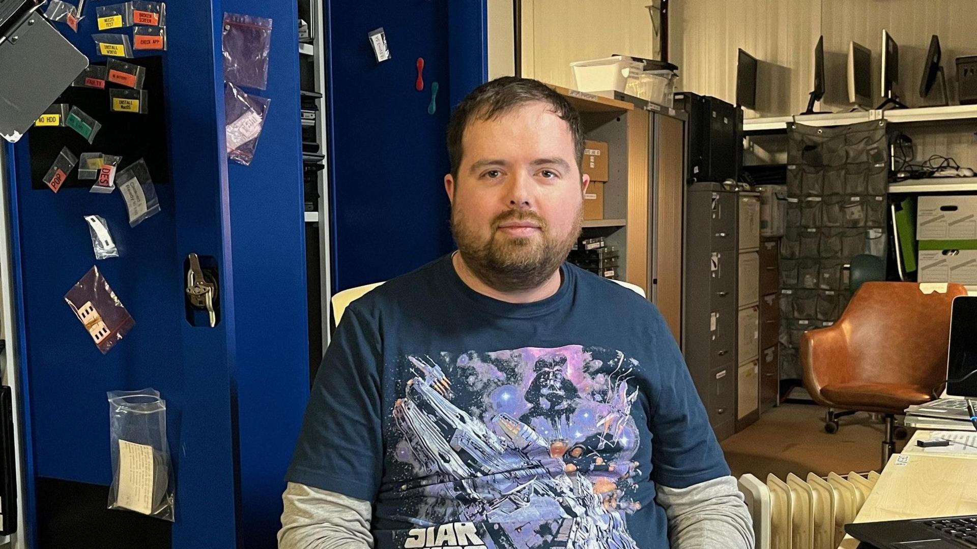 Daniel Lee looks at the camera. He has short, dark brown hair and dark facial hair. He is wearing a navy blue Star Wars t-shirt.