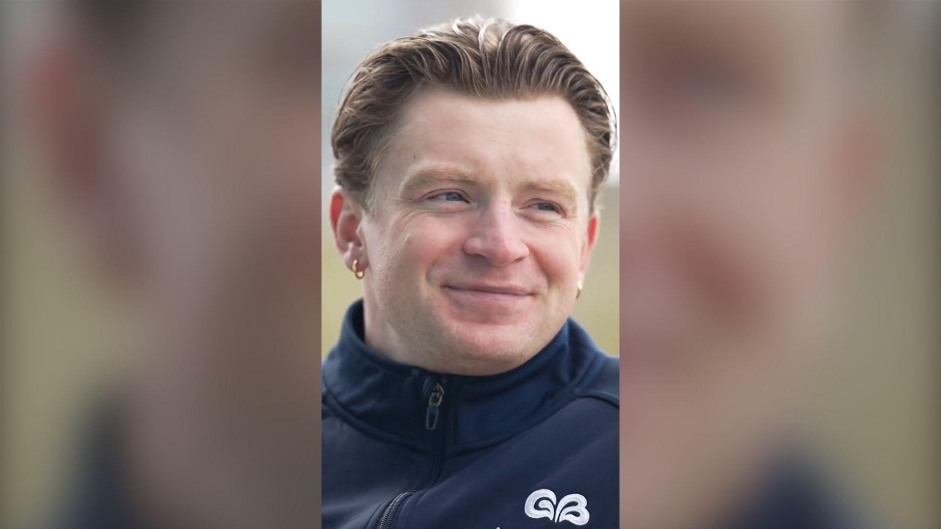 Adam Peaty looks to the side of the camera and smiles. He wears a navy jacket.