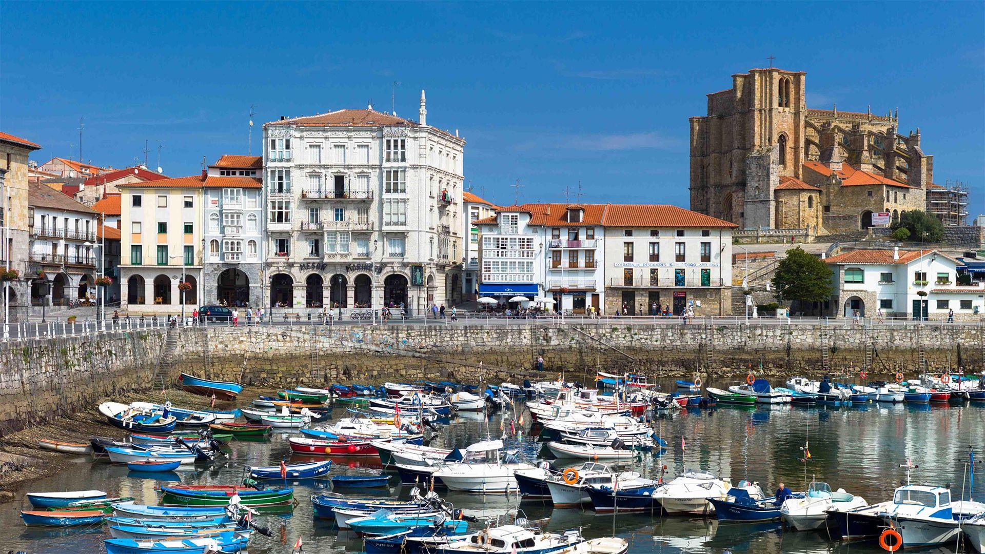 The church of Santa María de la Asunción overlooks the fishing harbour of Castro Urdiales in northern Spain. Moored fishing boats can be seen in the foreground while quayside buildings and the church can be seen in the background.