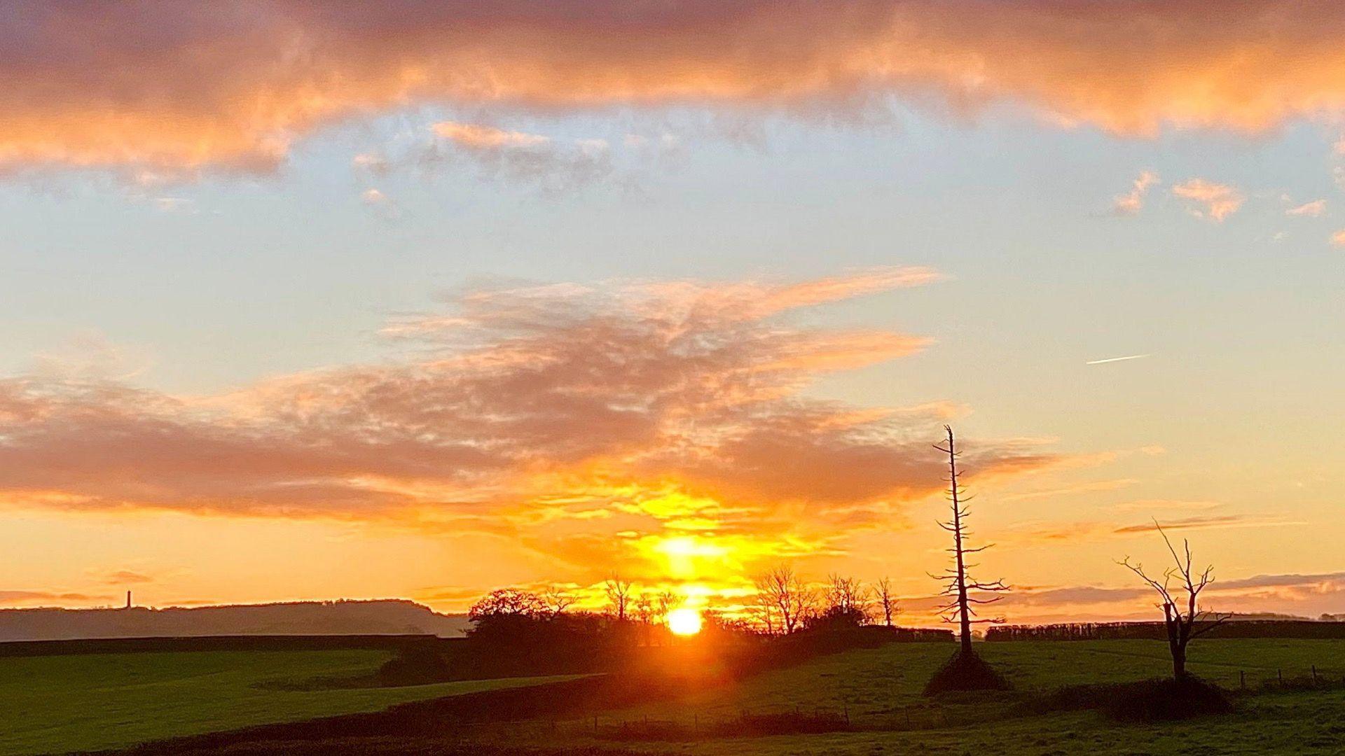 Sunrise with orange sky/clouds and green fields in the foreground at Berkeley in Gloucestershire