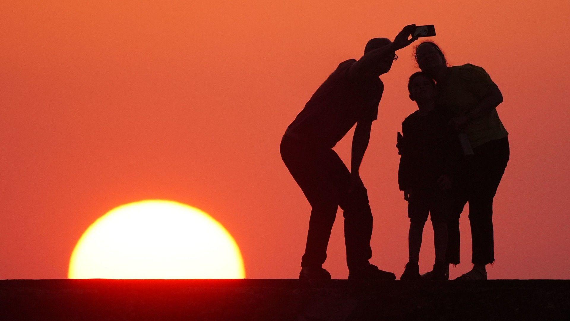 Three people taking a selfie silhouetted against a deep orange sky with the Sun rising on the horizon.