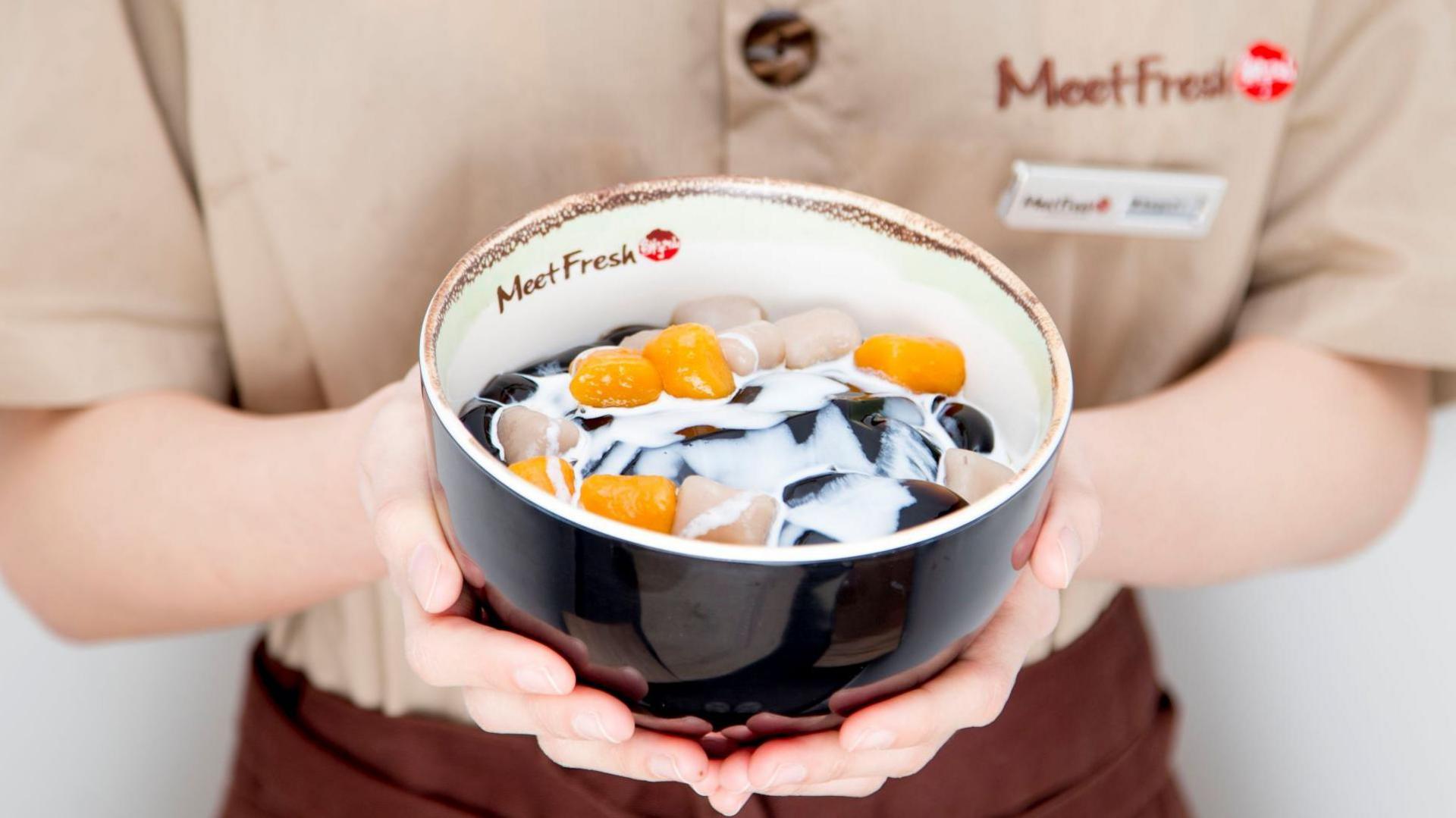 A bowl of colourful dessert being held by a Meet Fresh employee in a beige top and brown apron