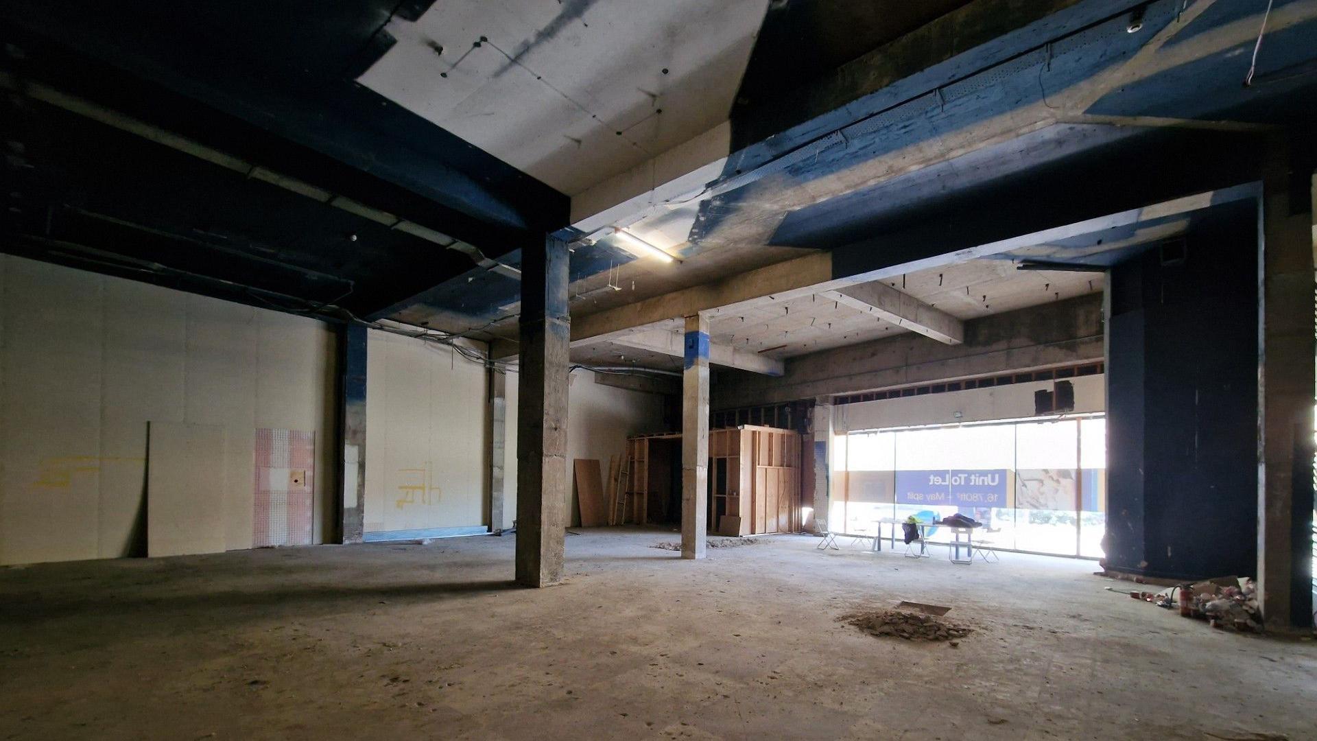 The inside of an empty building with concrete pillars and a window out onto the road