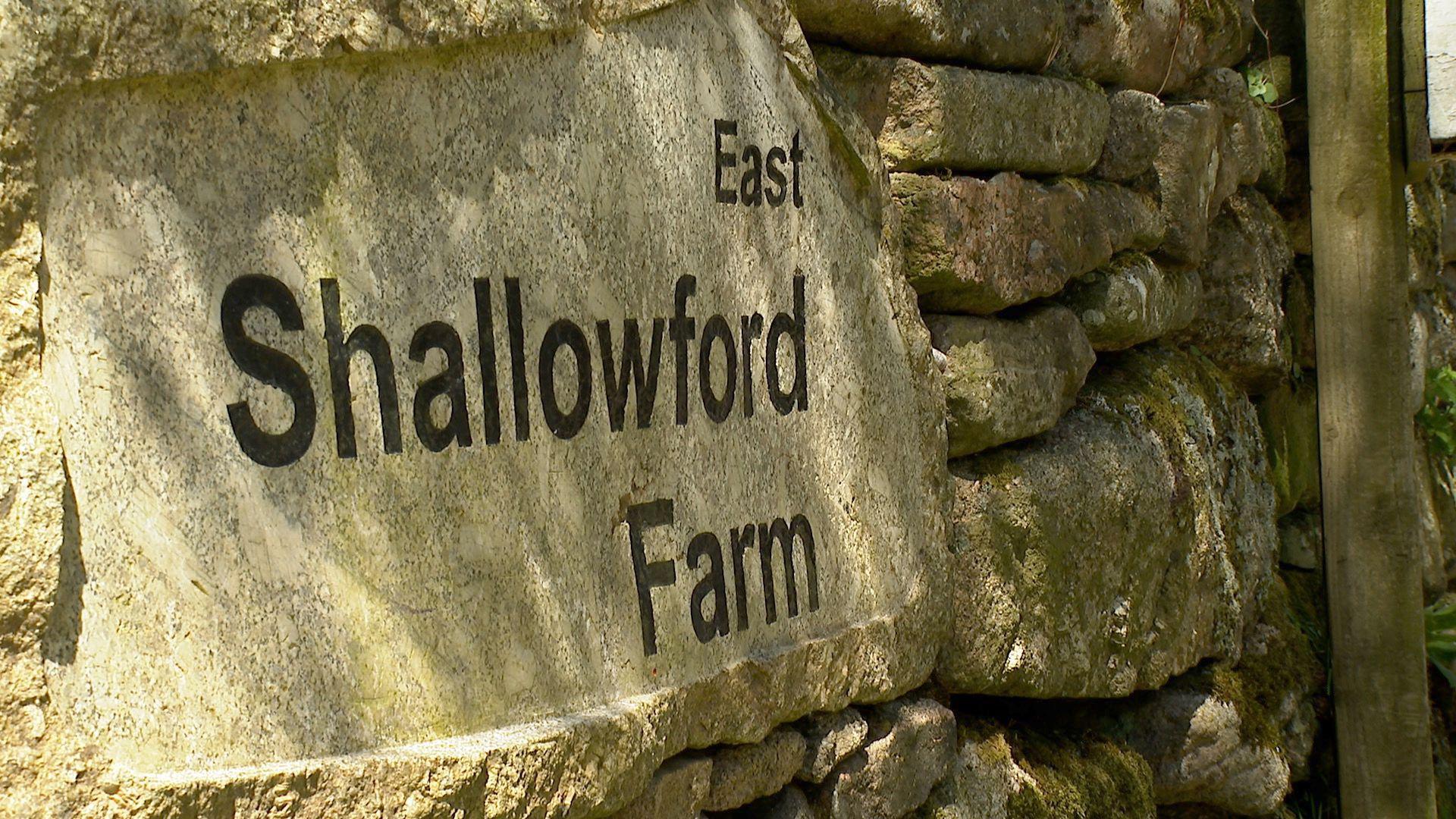 A close up of the sign for East Shallowford Farm on a traditional stone wall.