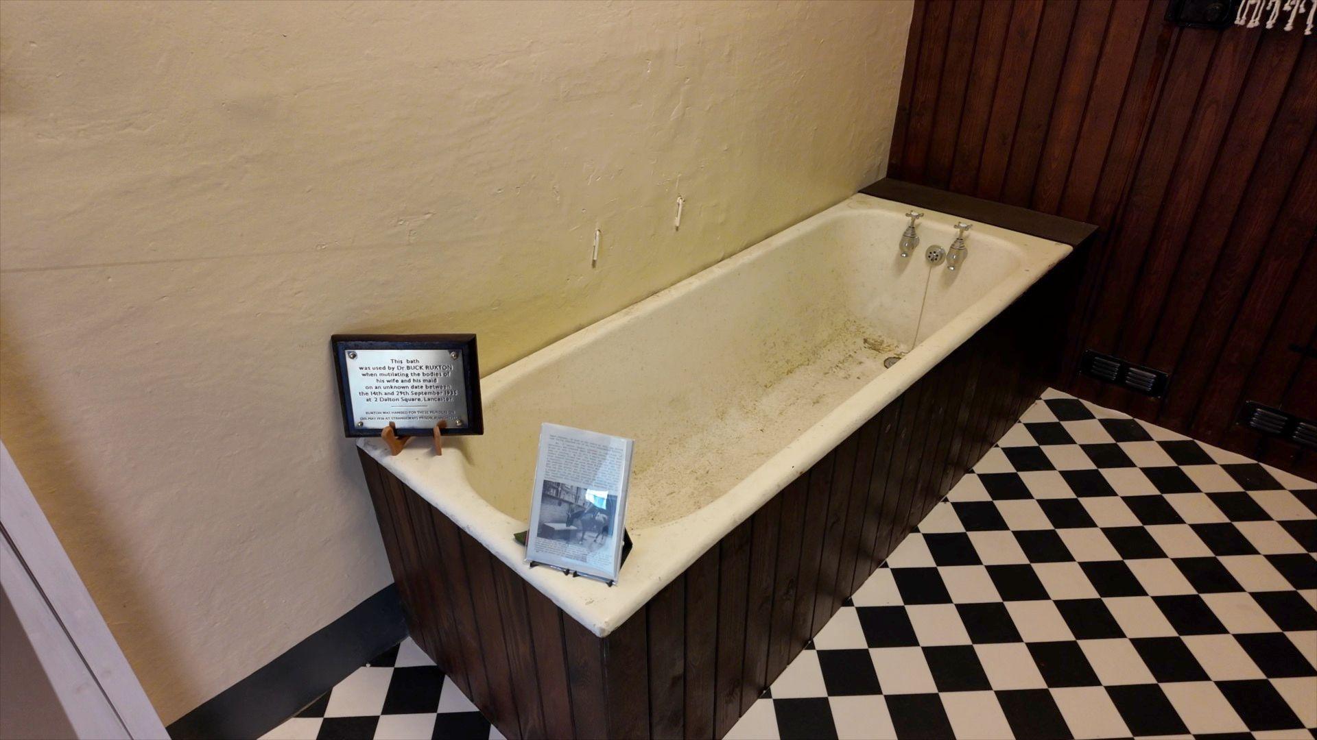 The original bath tub is now fitted in a reconstructed bathroom setting at Lancashire Policing Museum. It has dark wood panelled walls and a black-and-white tiled floor.