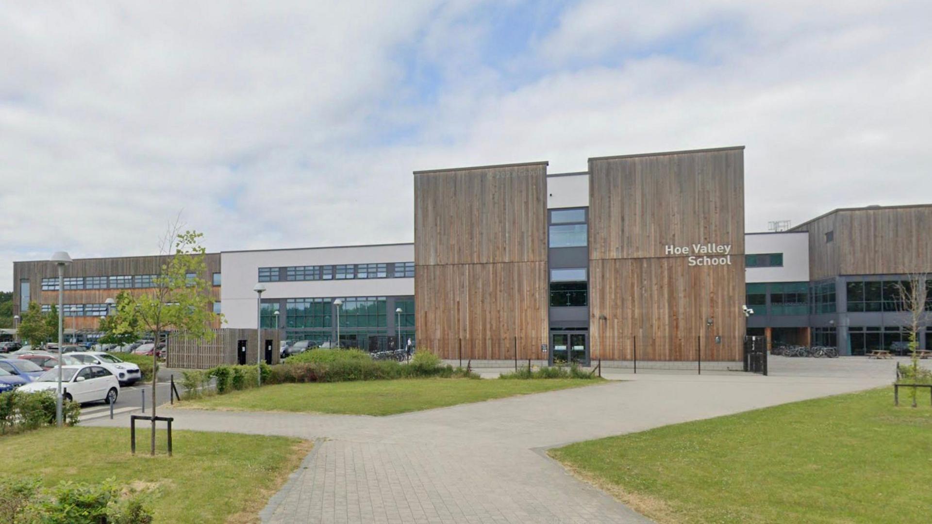 The outer buildings at Hoe Valley School in Woking. There is an area of grass and pavements in front of the school. 