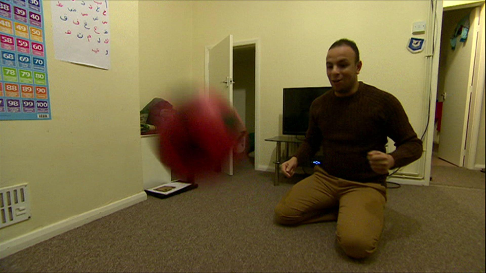Fahd is heading a football to his son in their living room