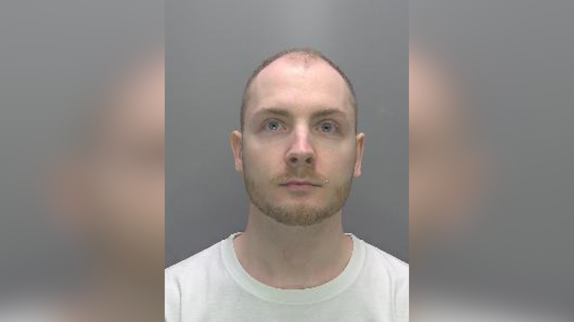 A mugshot of Thurston, who wears a white T-shirt and has a stubbled brown moustache and beard. He stares at the camera.