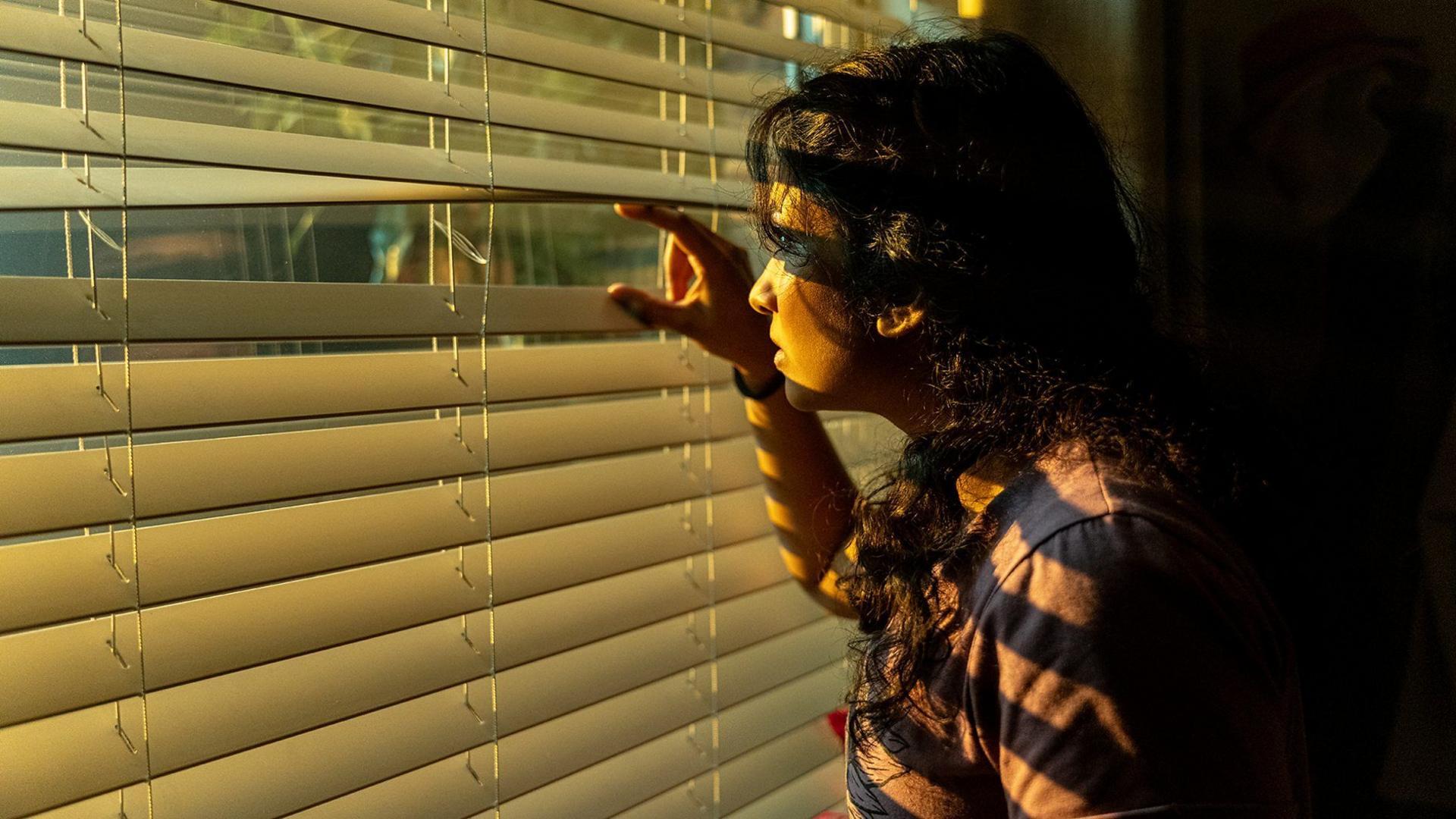 A person looking through some blinds.