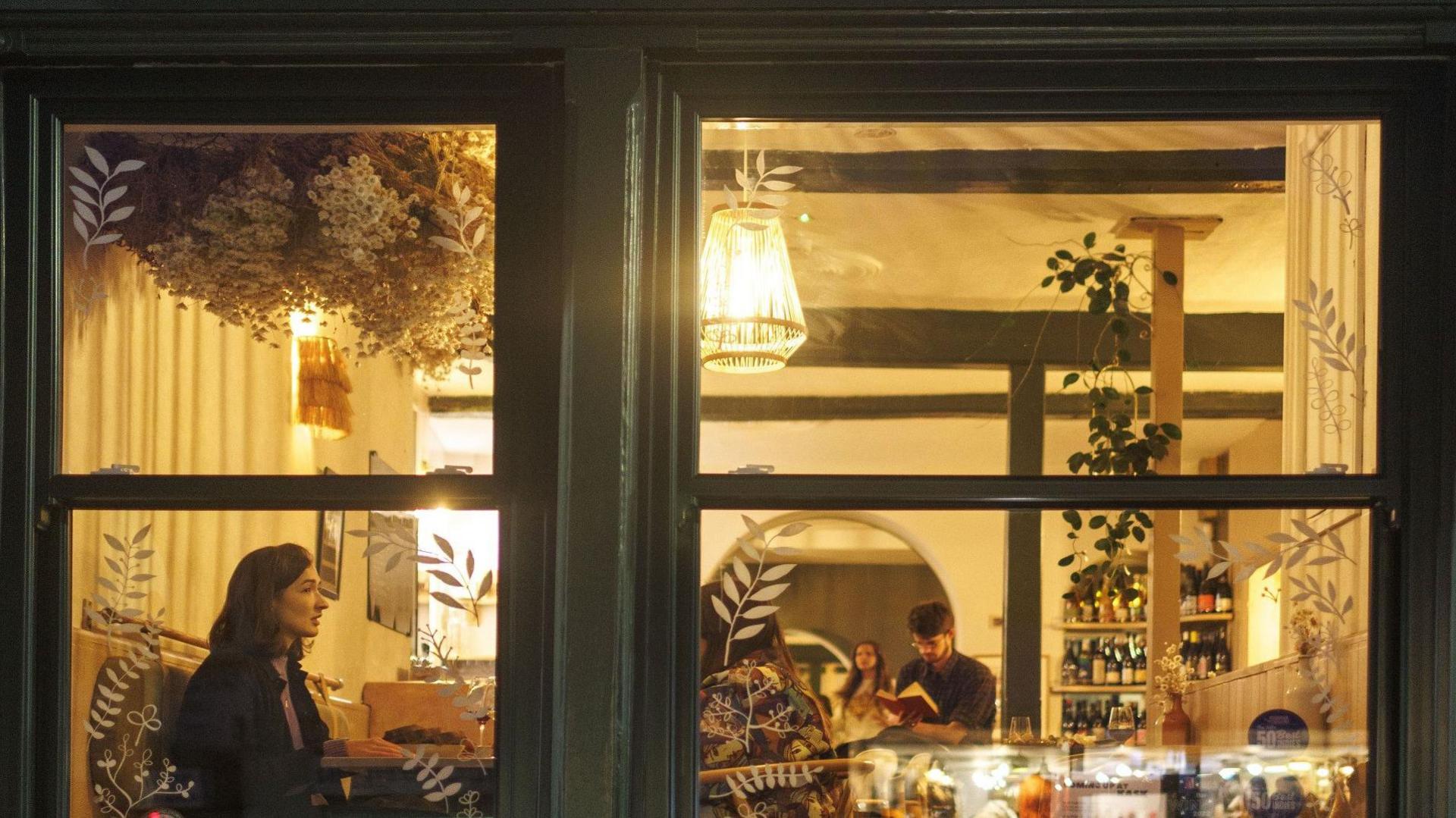 A young woman sits in an illuminated window in a wine bar called Kask in Bedminster in Bristol.