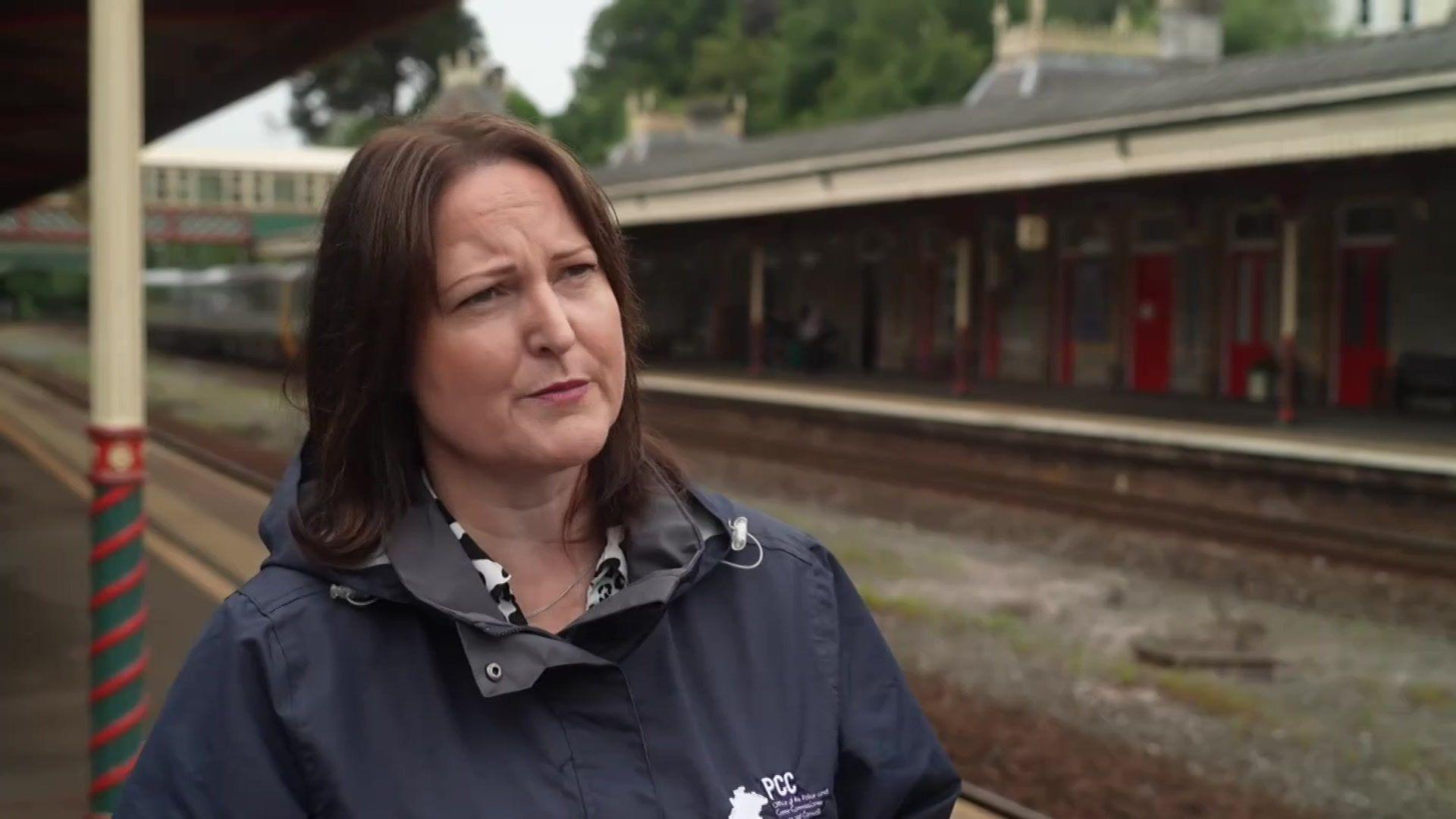 A picture of Alison Hernandez standing at a train station. She is wearing a black coat and has brown hair.