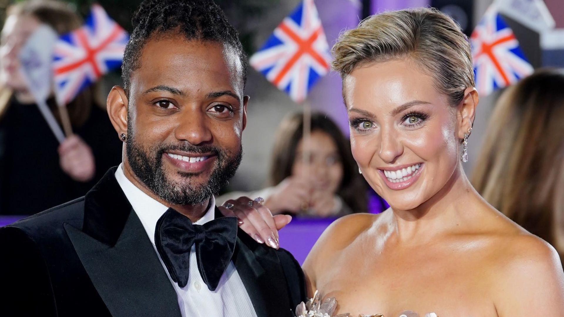 JB Gill wearing a tux and black velvet bow tie poses alongside Amy Dowden who is wearing a strapless dress.