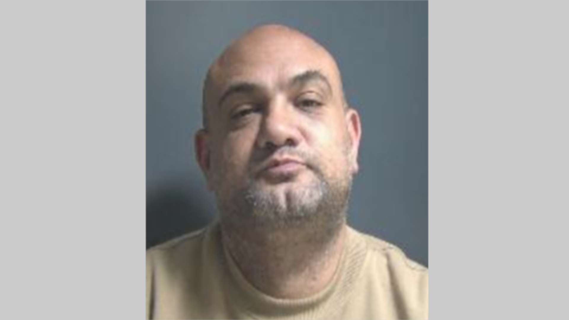 Ashley McNeil has his head tilted upwards and is looking directly at the camera. He is wearing a beige jumper and has stubble across his chin. 