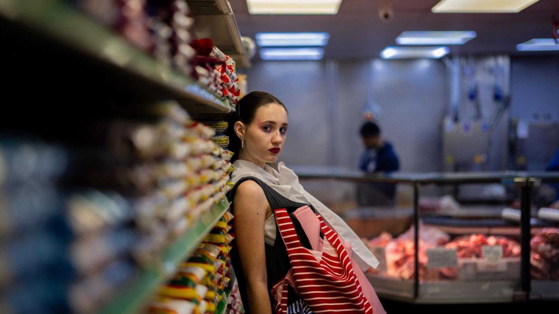 A female model leaning against some shelves in a corner shop.