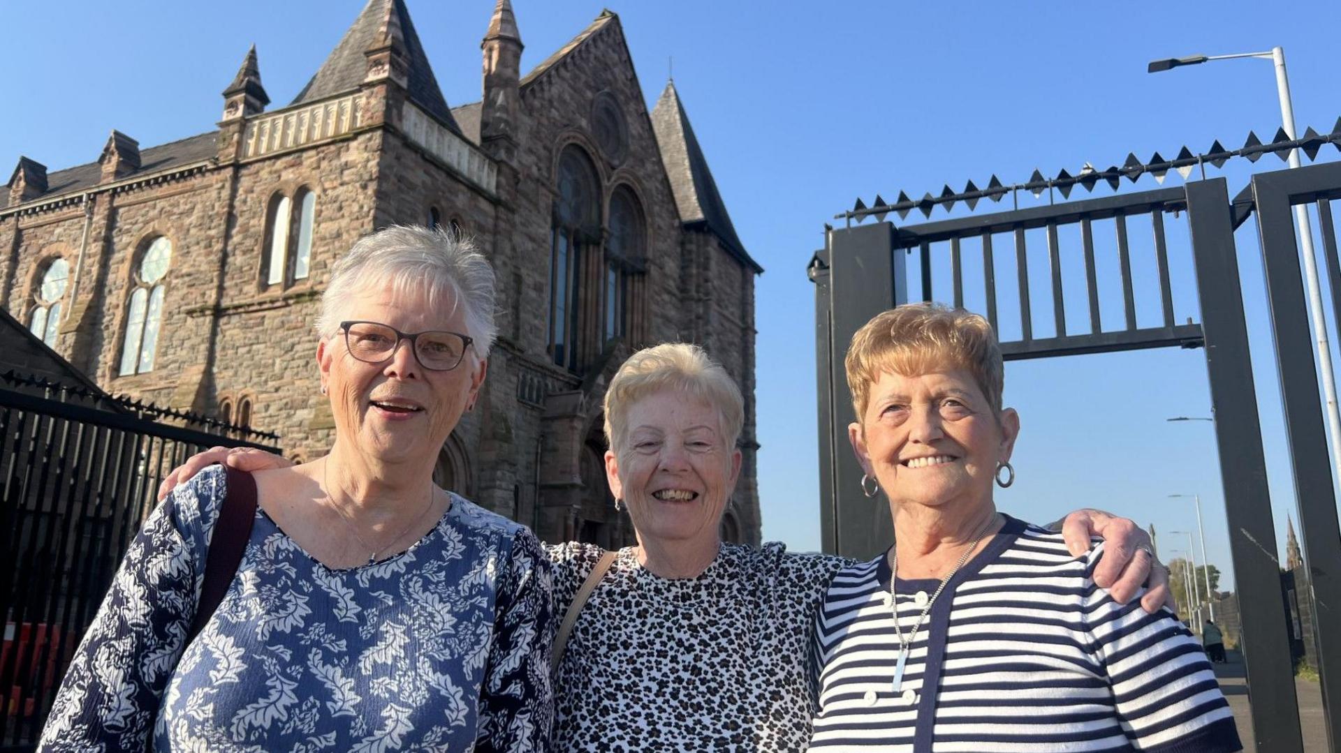 Three women standing. On the far left women is wearing blue and white top. In the middle a women in a cheetah print top and on the right a blue and white stripe top. 