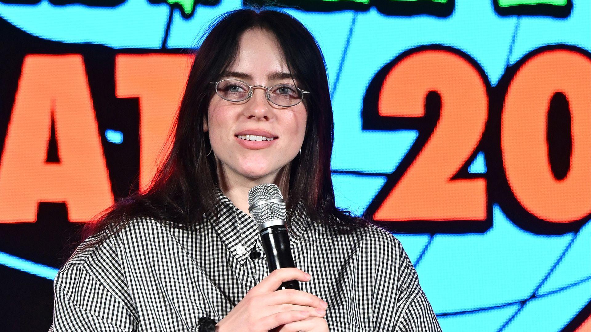 Billie Eilish holds a microphone and speaks at an event.