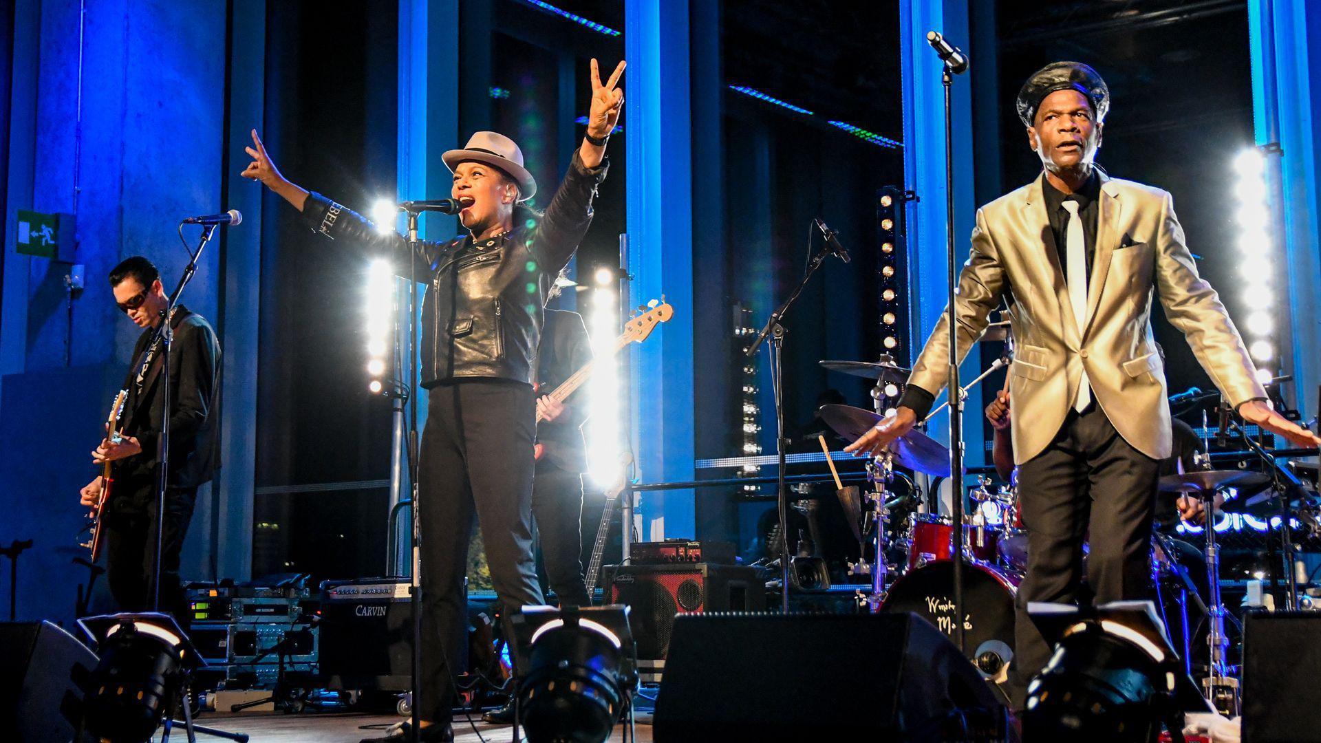 The Selecter performing on stage. The lead singer, called Pauline Black, is making the international peace symbol with both hands.